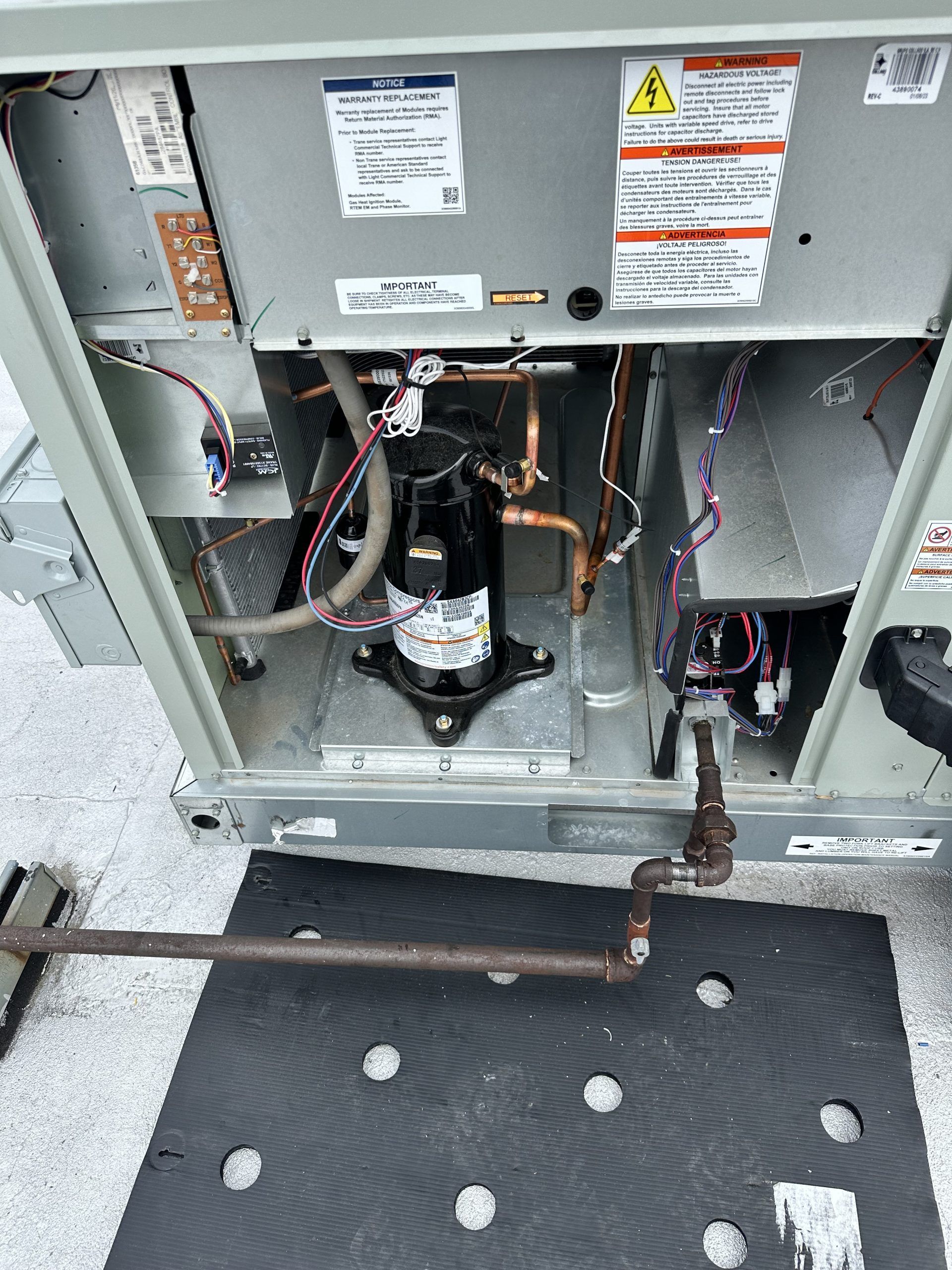 Opened air conditioning unit showing a compressor and copper piping. Gray metal, black and brown components.