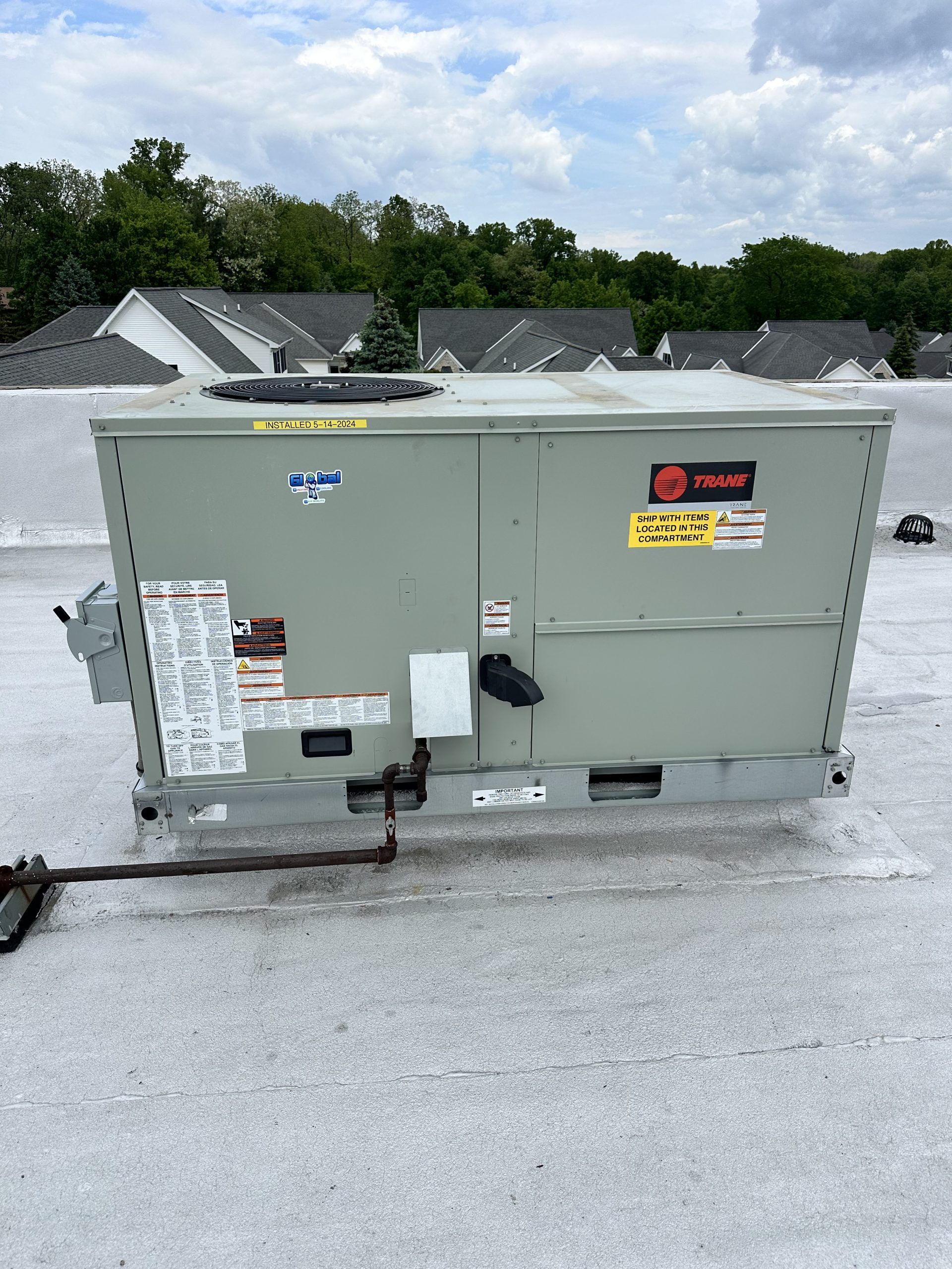 Large, gray rooftop HVAC unit with various warning labels, pipes, and access panels against a cloudy sky.