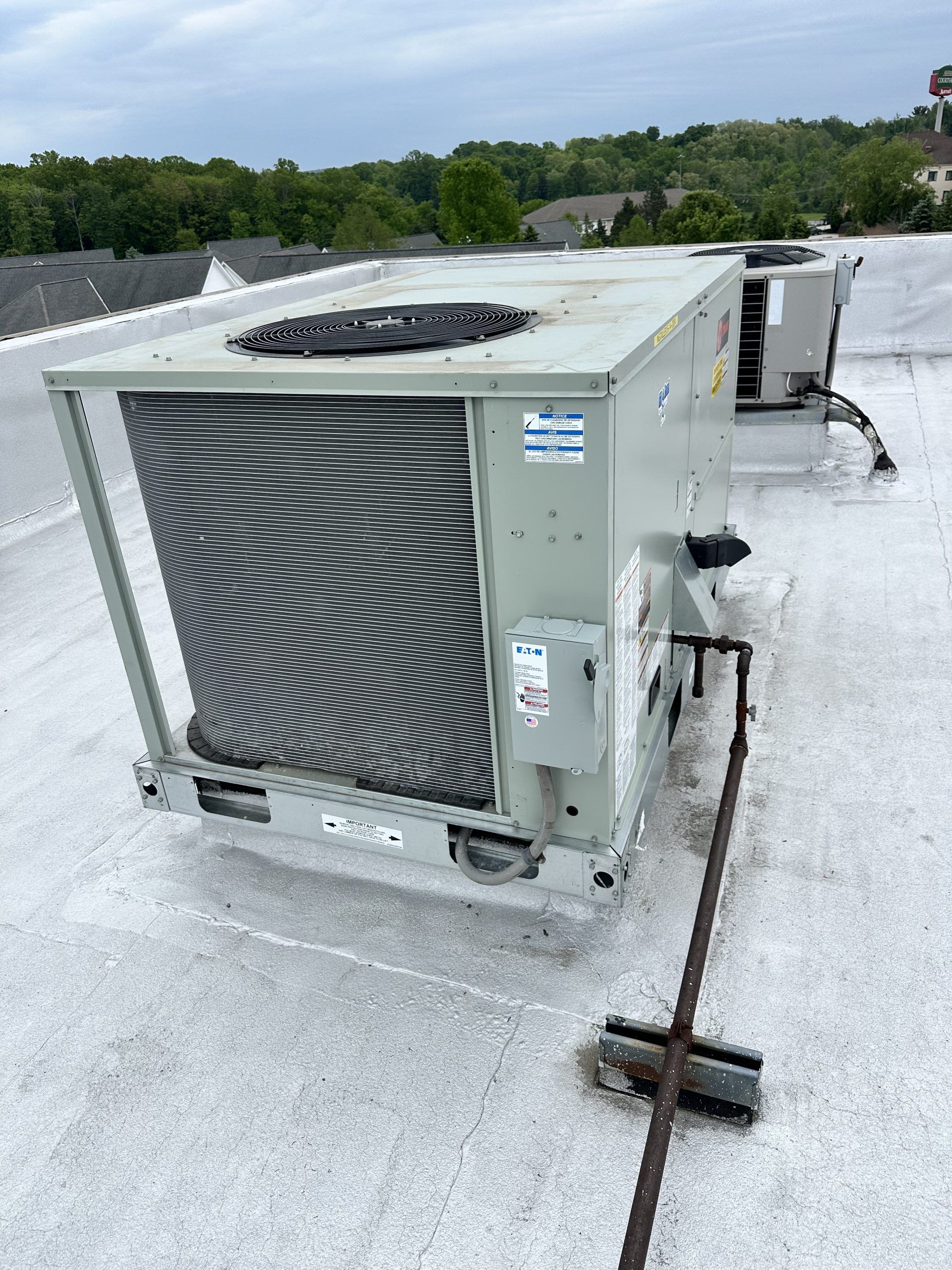 HVAC unit on a flat white roof with trees and sky in the background. A broom rests nearby.