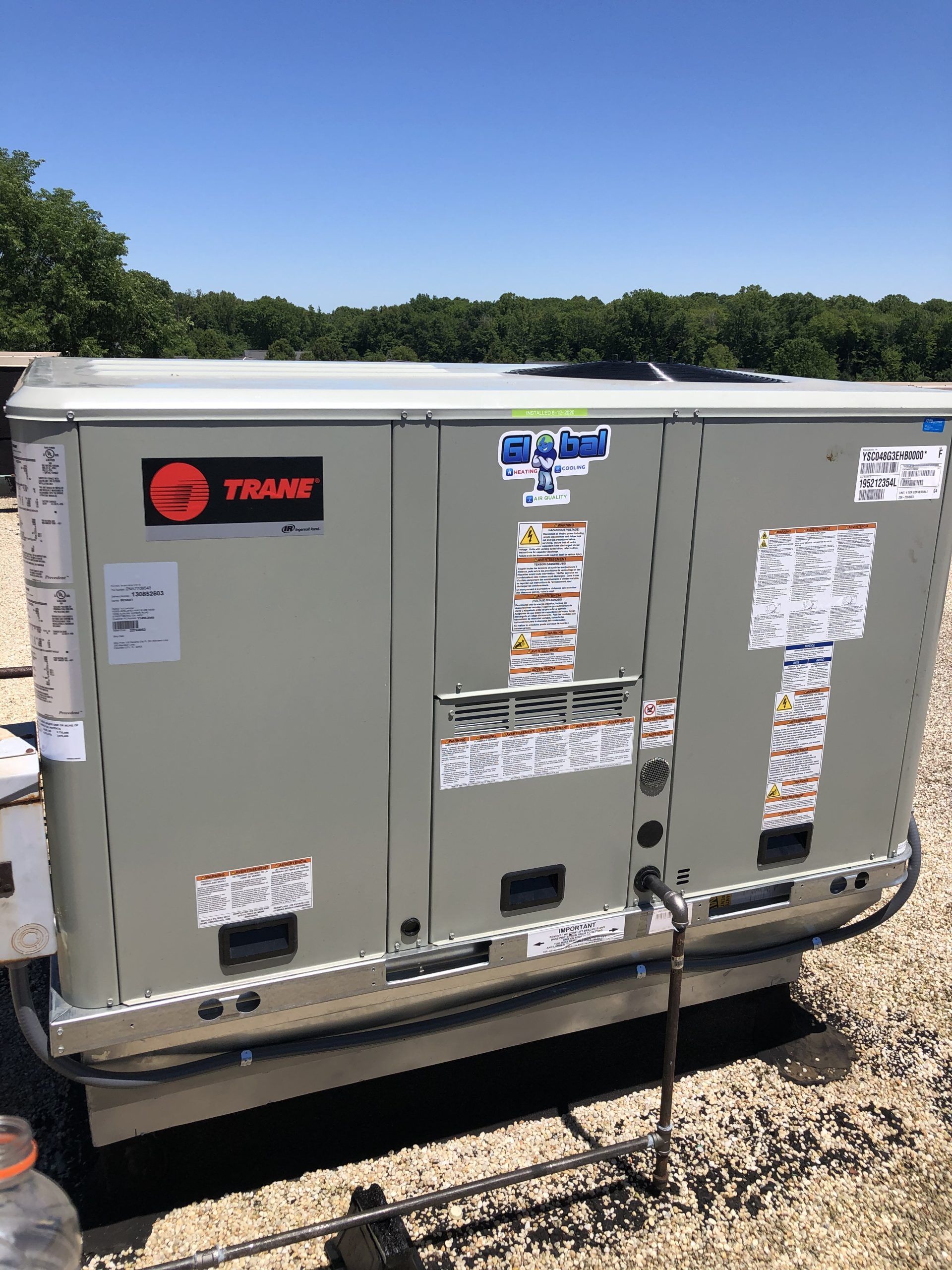 A Trane rooftop HVAC unit on a gravel surface under a blue sky.