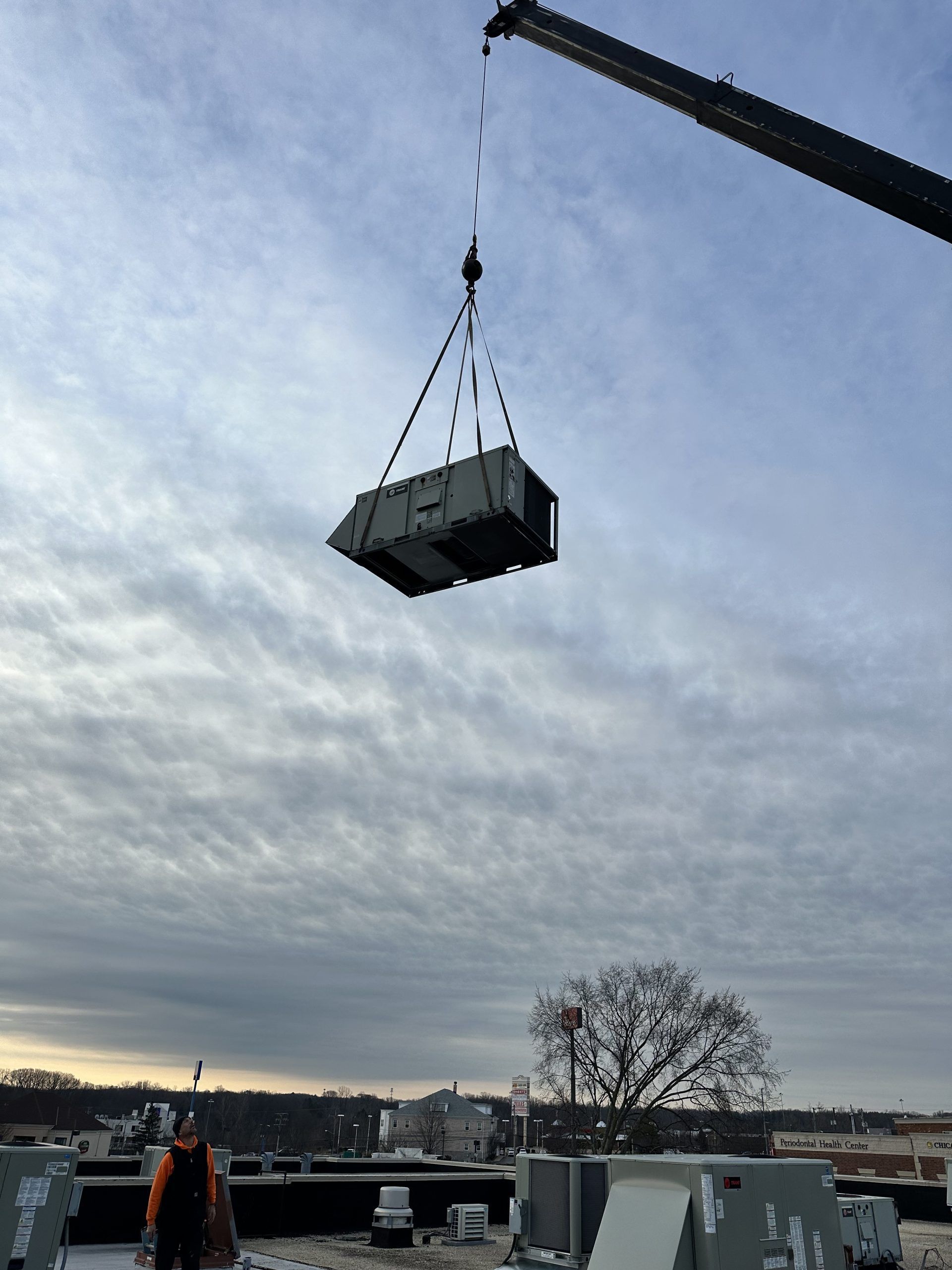 A crane lifting an HVAC unit onto a rooftop. Cloudy sky in the background.