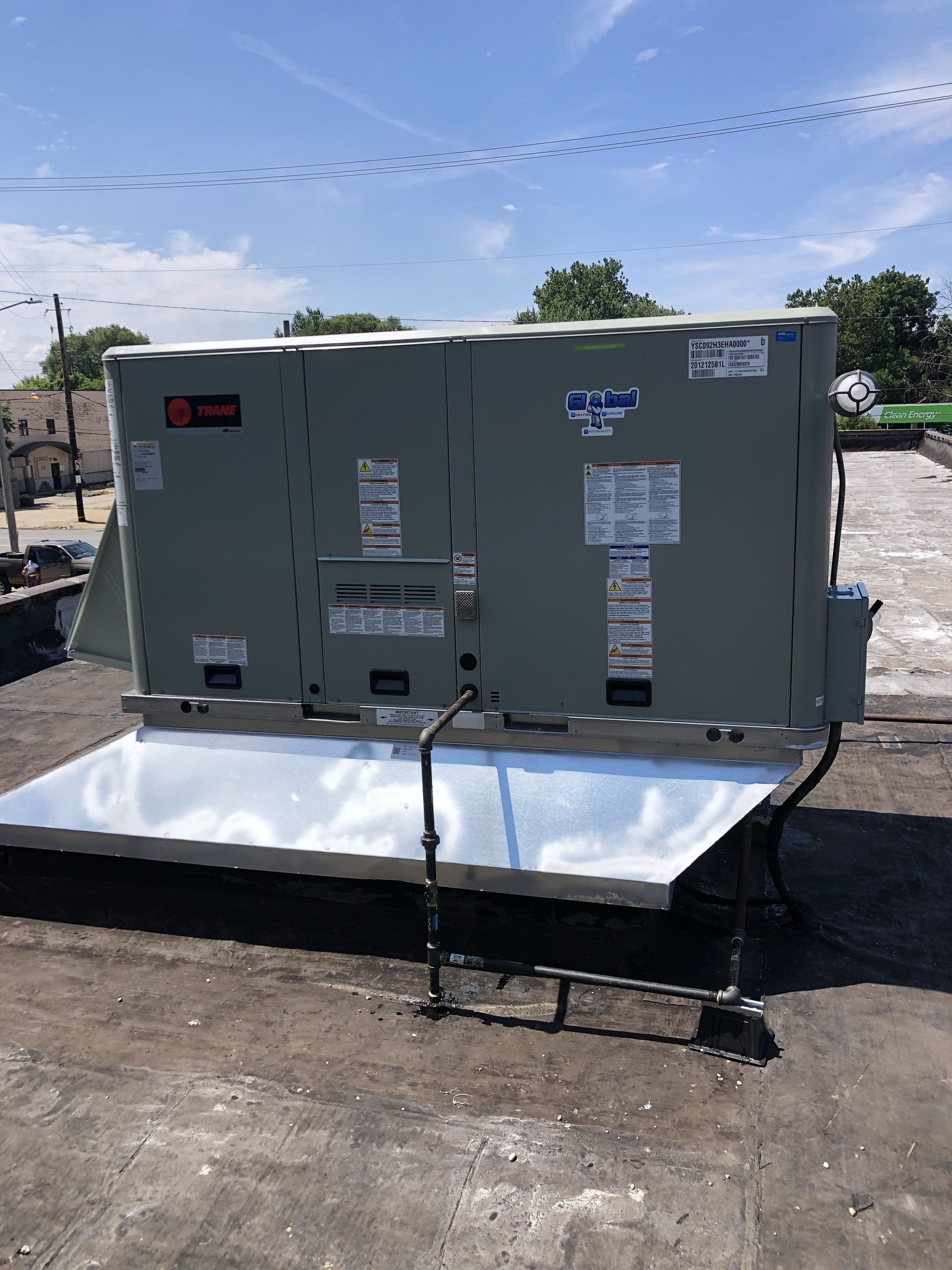 A large, gray rooftop HVAC unit on a flat, dark roof under a bright blue sky.
