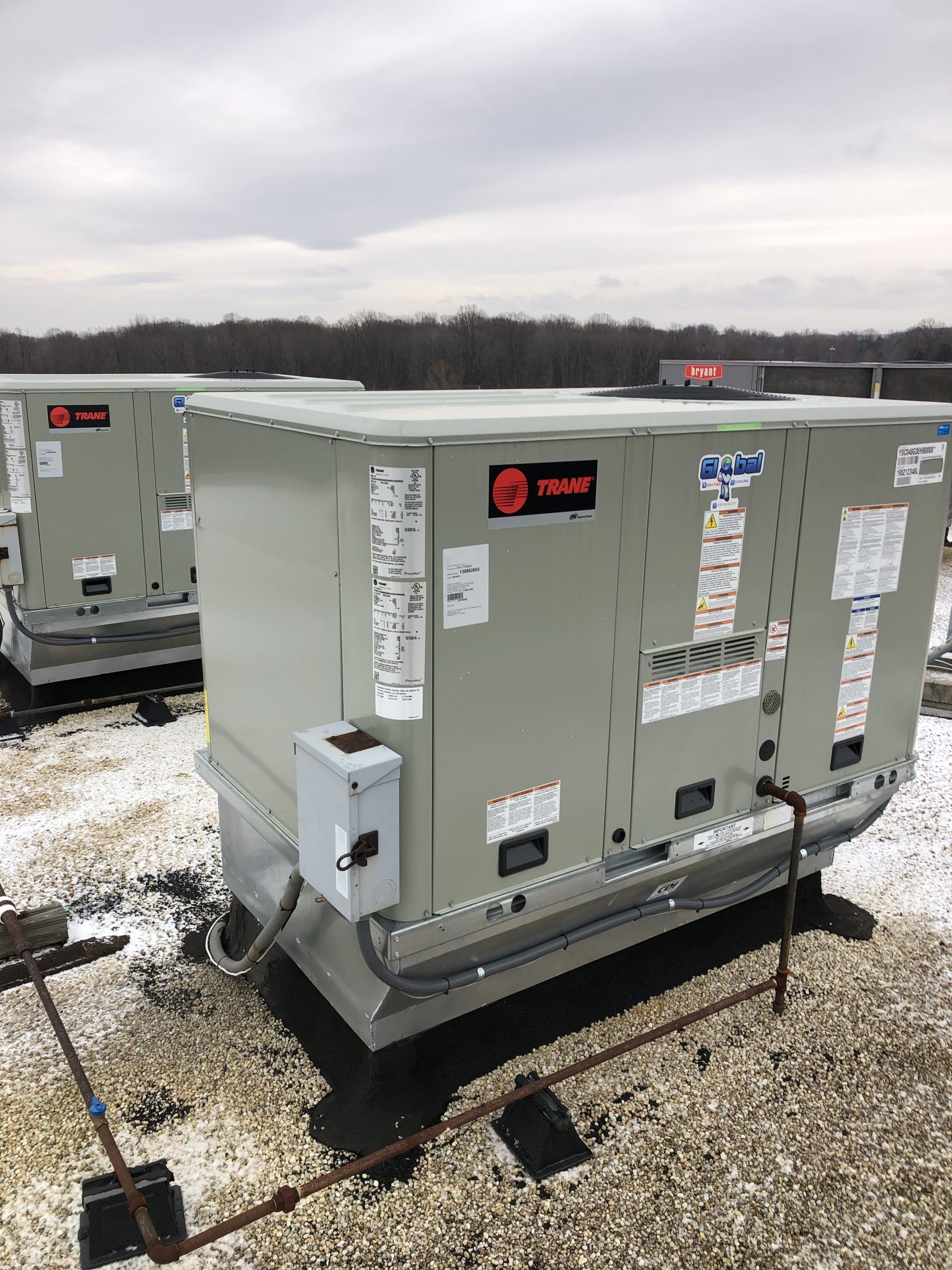 Two rooftop HVAC units on a cloudy day. Gray metal boxes with Trane logo and control panels.