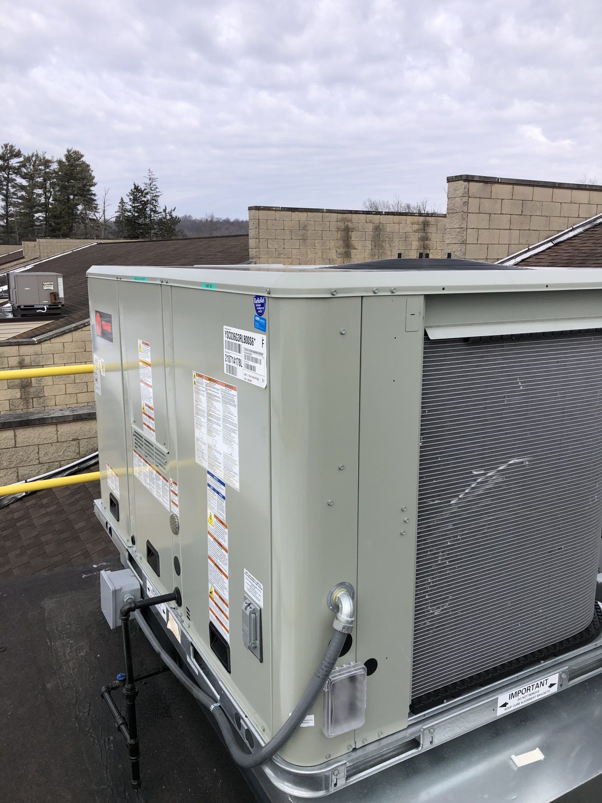 Gray HVAC unit on a rooftop, with labels and a protective grate, against a cloudy sky.