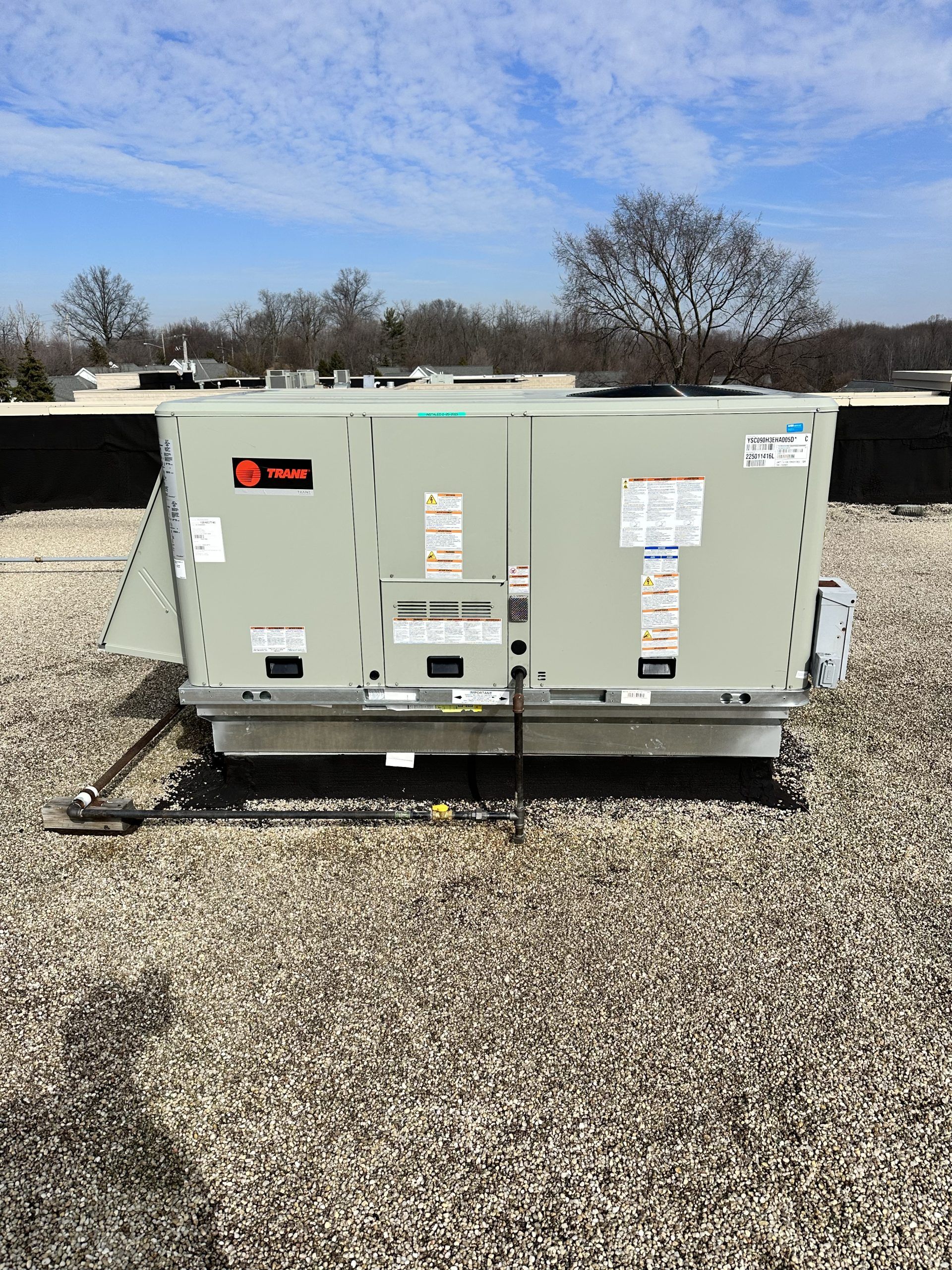 Rooftop HVAC unit on a flat roof under a blue sky, Trane logo visible.