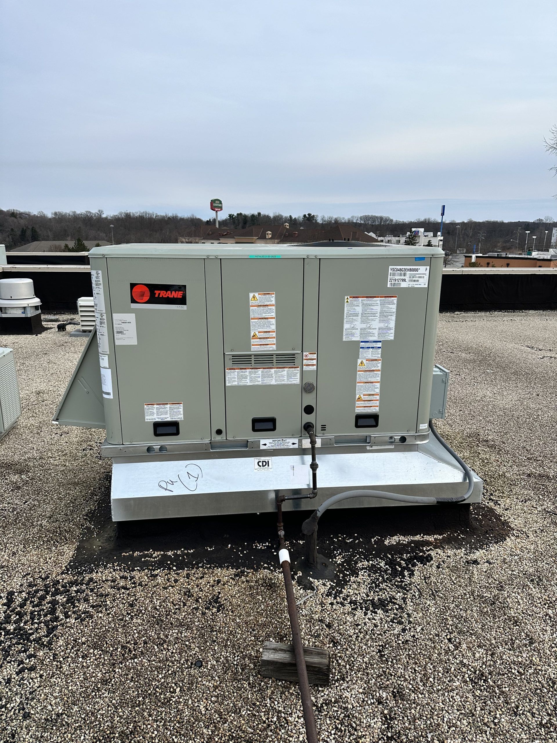 Rooftop HVAC unit on a gravel surface under a cloudy sky. The unit is gray with orange and blue labels.
