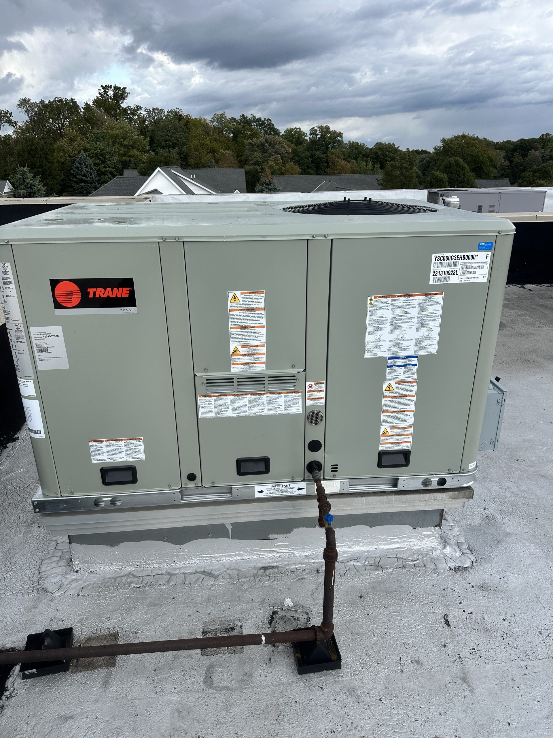 Gray Trane HVAC unit on a rooftop, with warning labels and dark grounding wire.