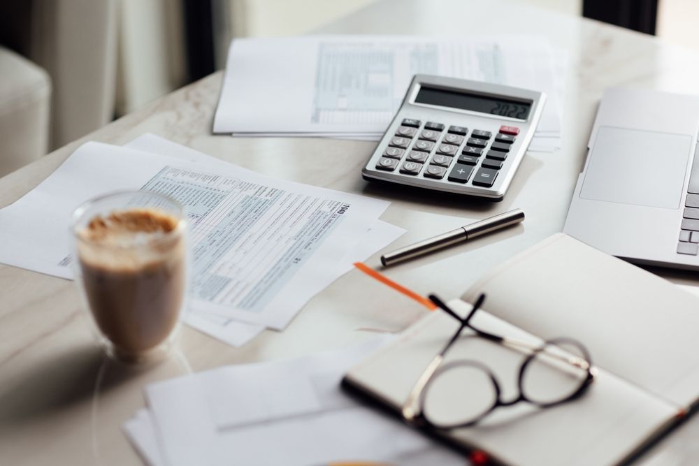 Desk with documents, calculator, pen, eyeglasses, coffee, and a notebook.