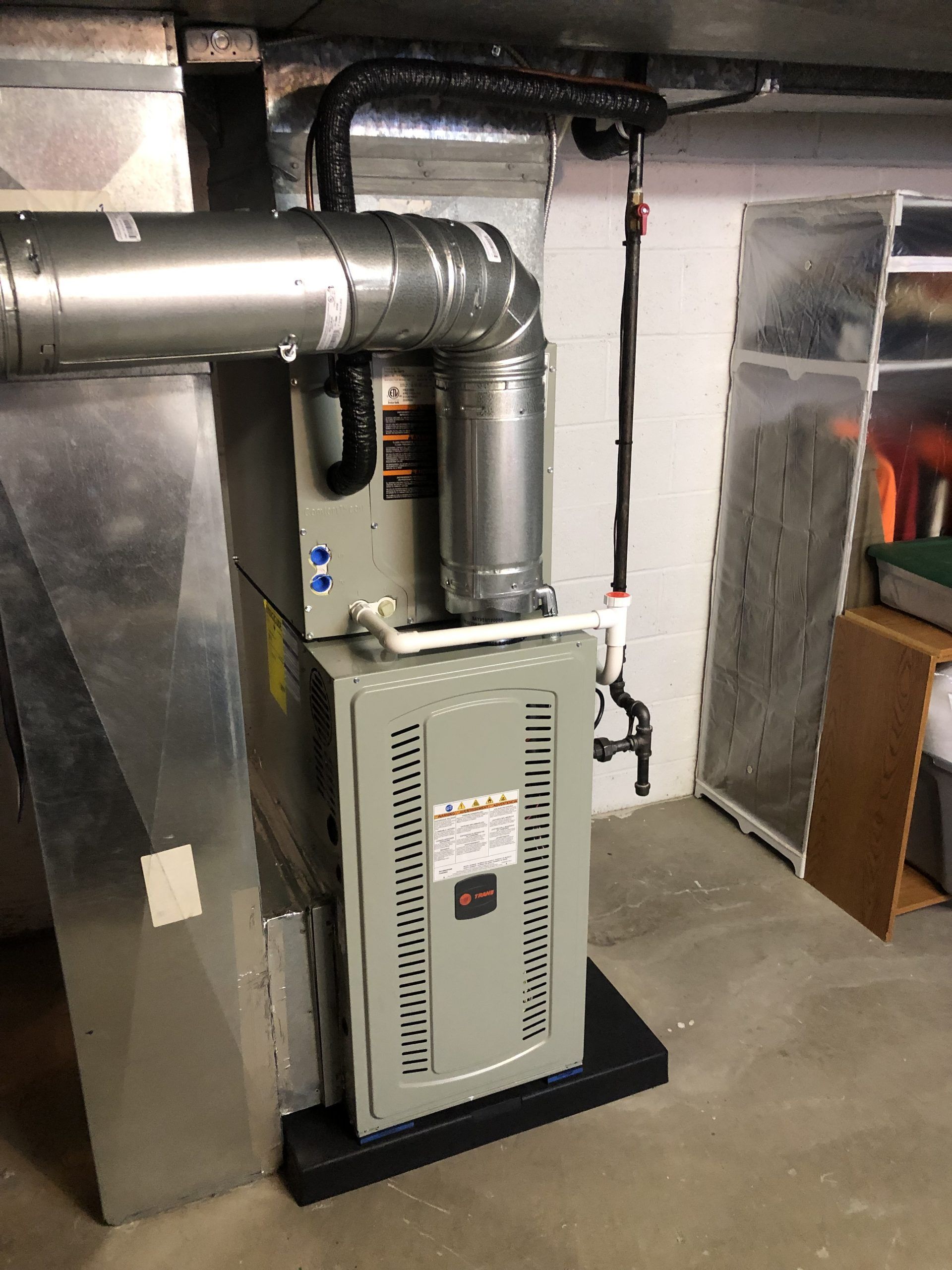 Furnace and ductwork in a basement setting. Gray and silver components against white walls and a concrete floor.