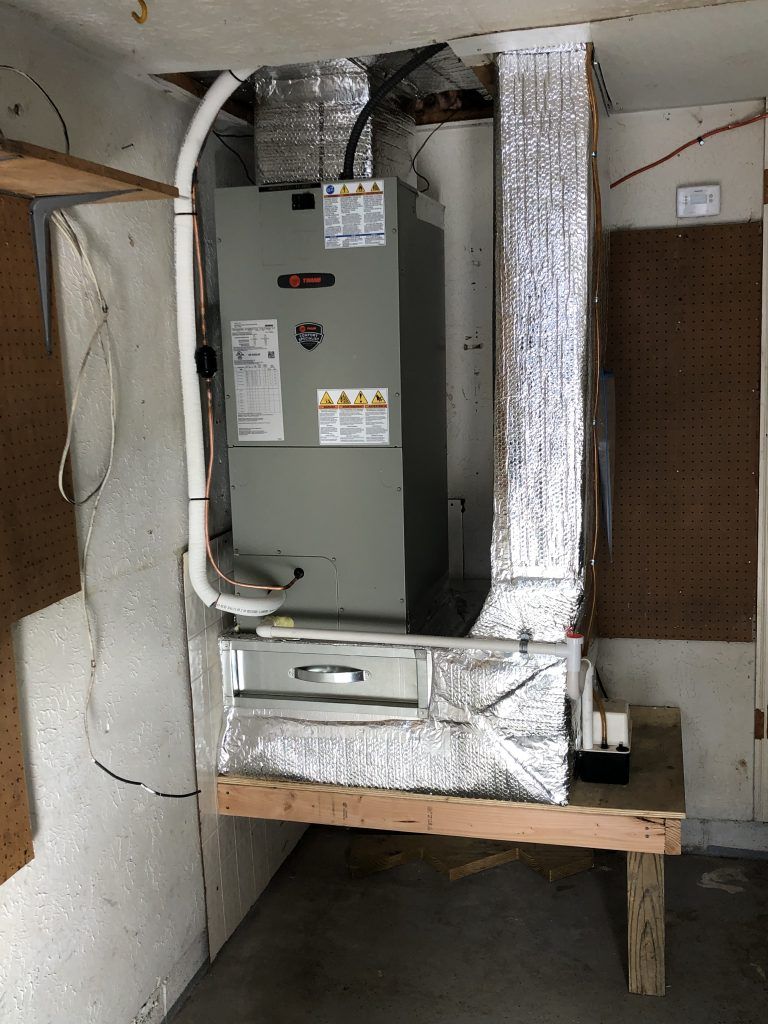Furnace unit in a garage, connected to ductwork. Metal and gray appliance.