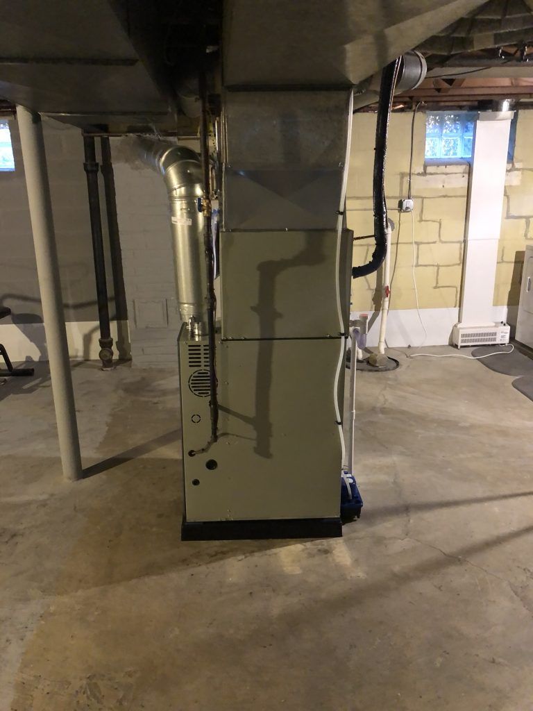 Furnace in a basement, silver metal, black pipe, and ductwork; concrete floor and block walls.