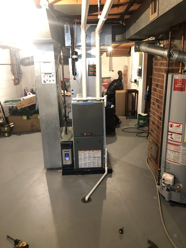 Basement with furnace and water heater. Gray floor, exposed beams and ductwork. White and gray appliances.