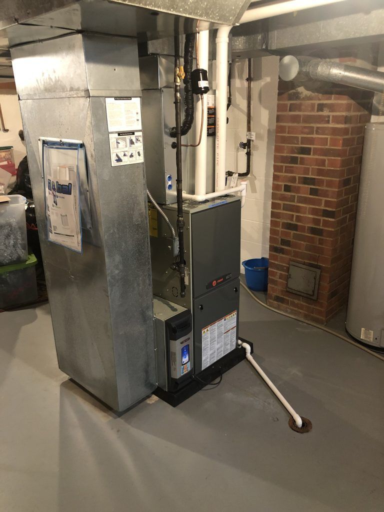 HVAC furnace unit in basement, connected to ductwork. Gray metal and a brick chimney visible.