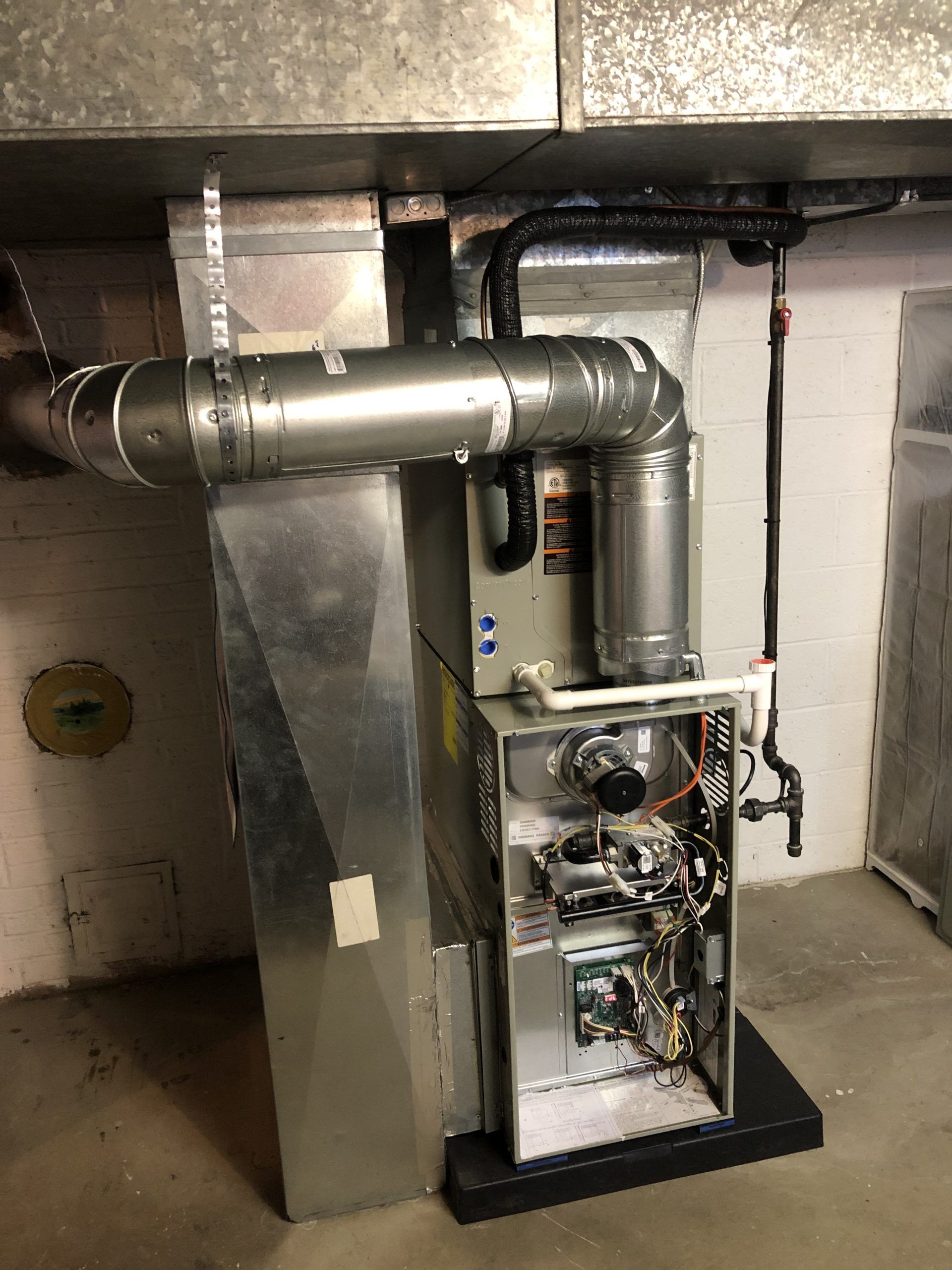 Furnace unit in a basement, with ductwork and open access panel revealing internal components.