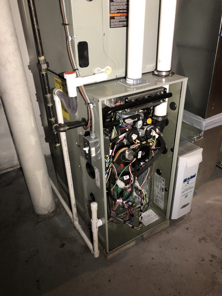 Furnace with open panels showing wiring and components in a basement setting.