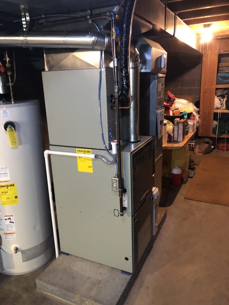 Furnace and water heater in a basement. Metal units, pipes, and utility labels are visible.
