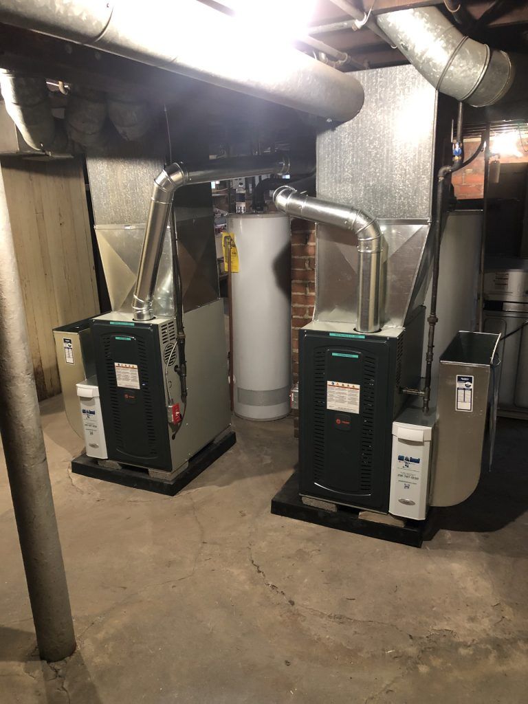 Two furnaces with attached ductwork in a basement setting.