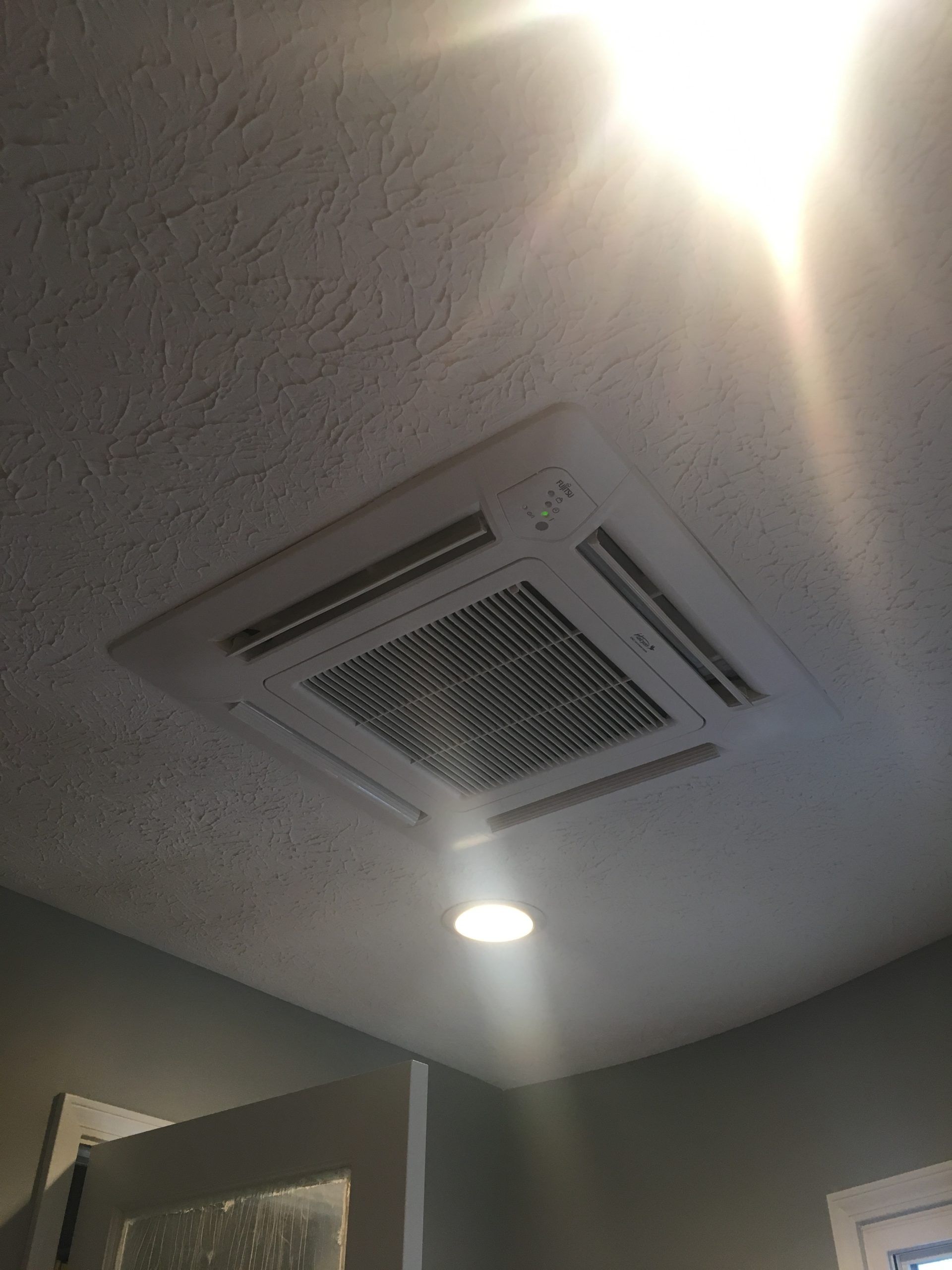 Ceiling-mounted air conditioning unit with vents, recessed lighting. White ceiling and trim, in a room.