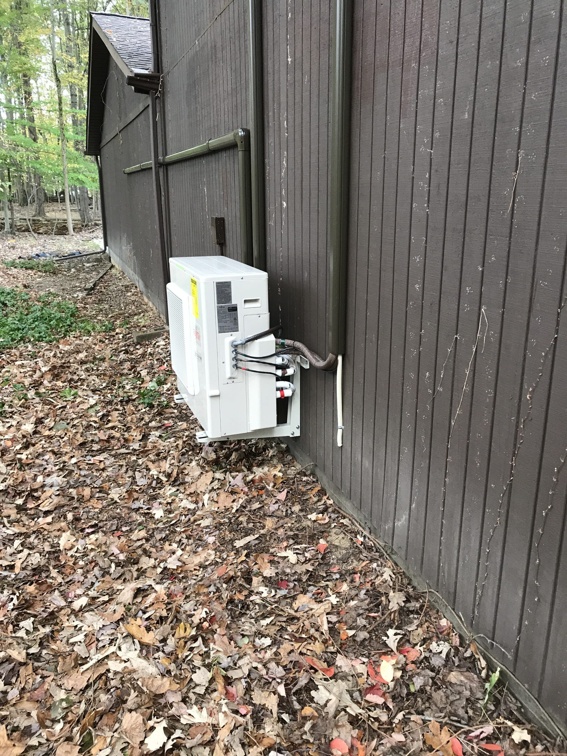 HVAC unit mounted on the exterior wall of a brown building, surrounded by fallen leaves.