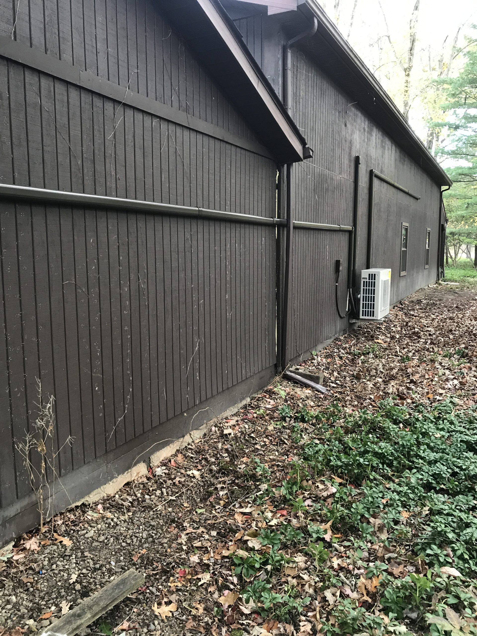 Brown wooden building exterior with vertical siding. A/C unit, gutter, and fallen leaves.