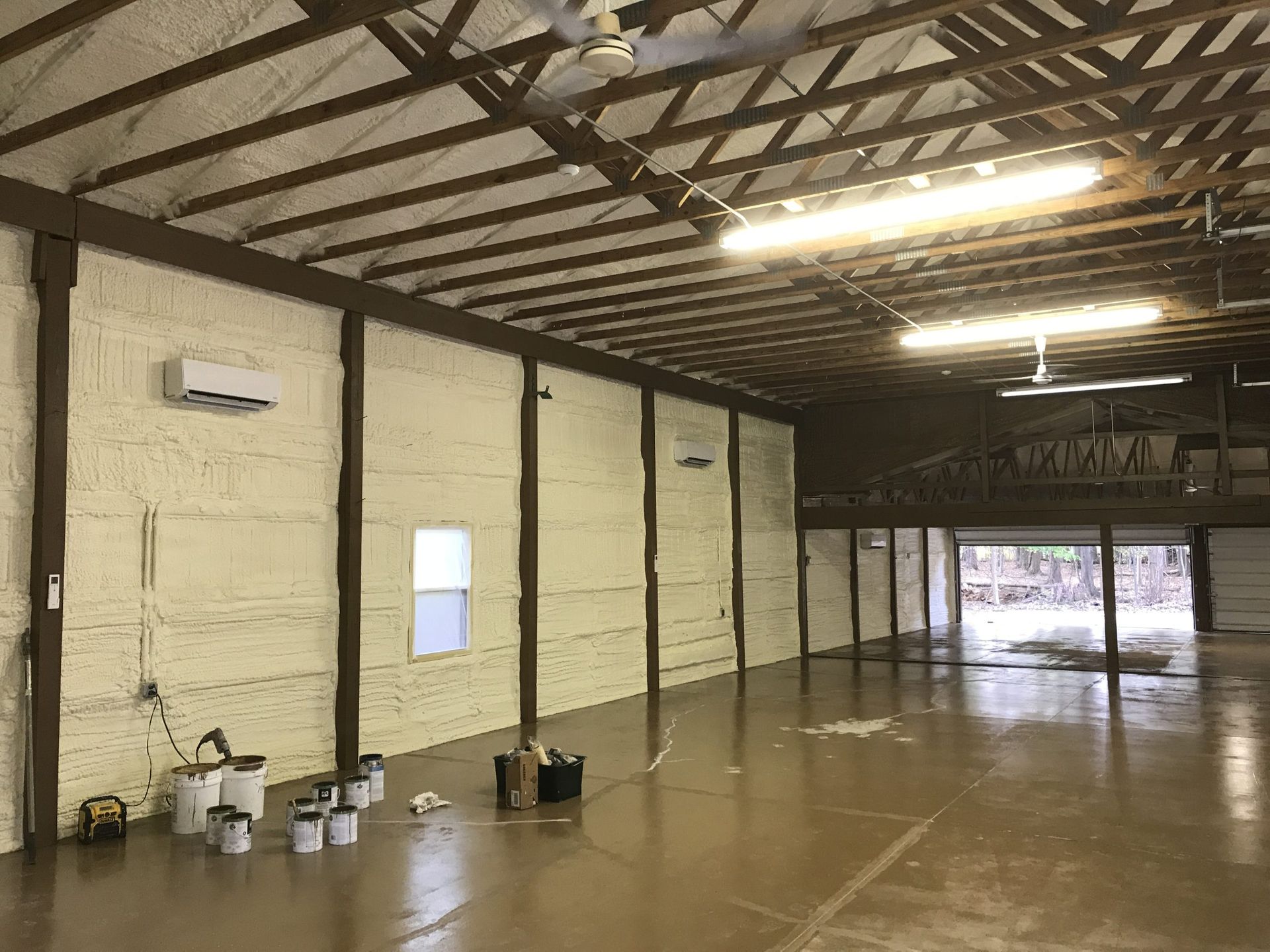 Interior of a large building with spray foam insulation on the walls and exposed wooden beams.