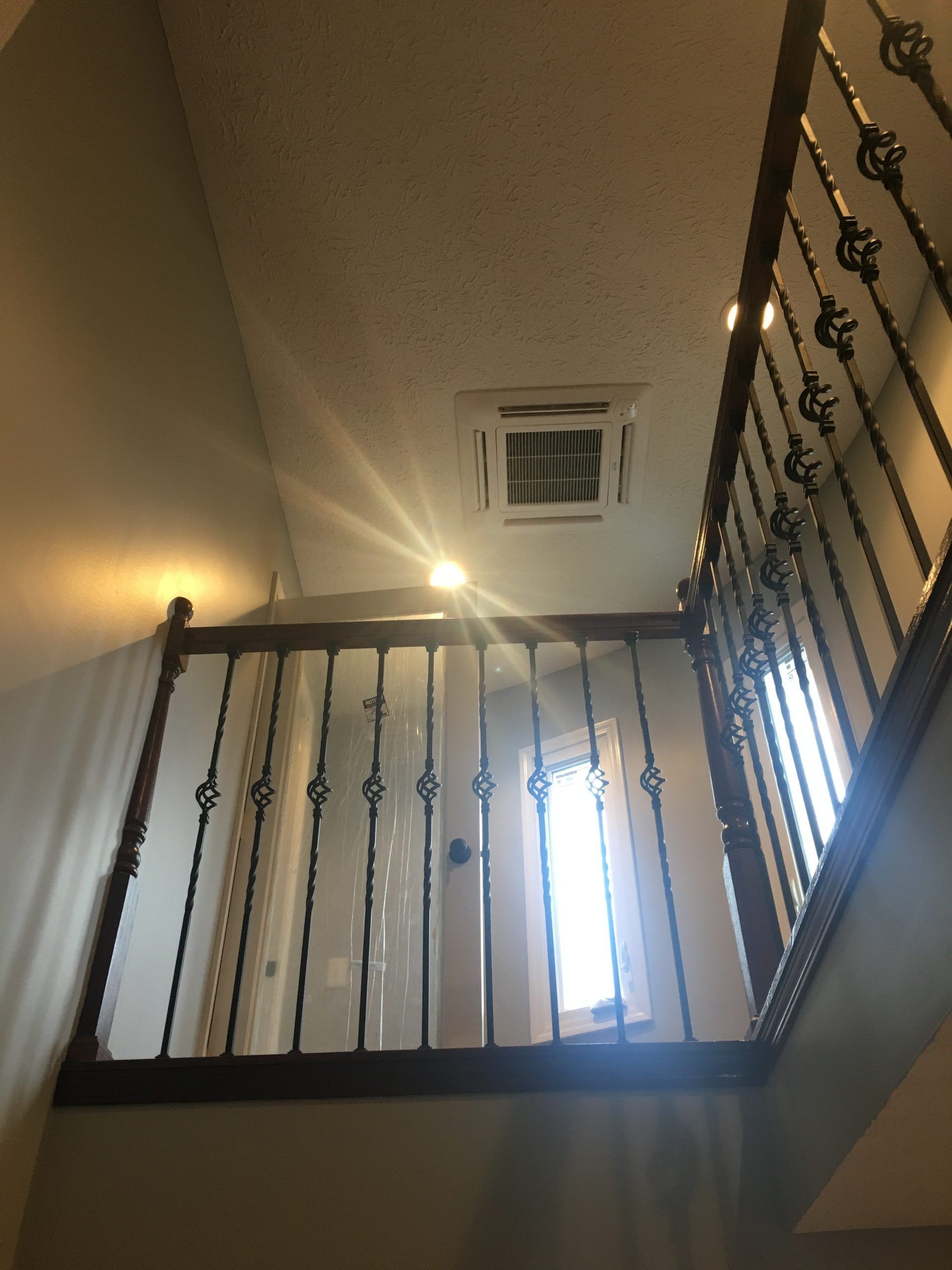 Stairwell with dark wooden railing and ornate metal balusters, sunlight shining from a window.