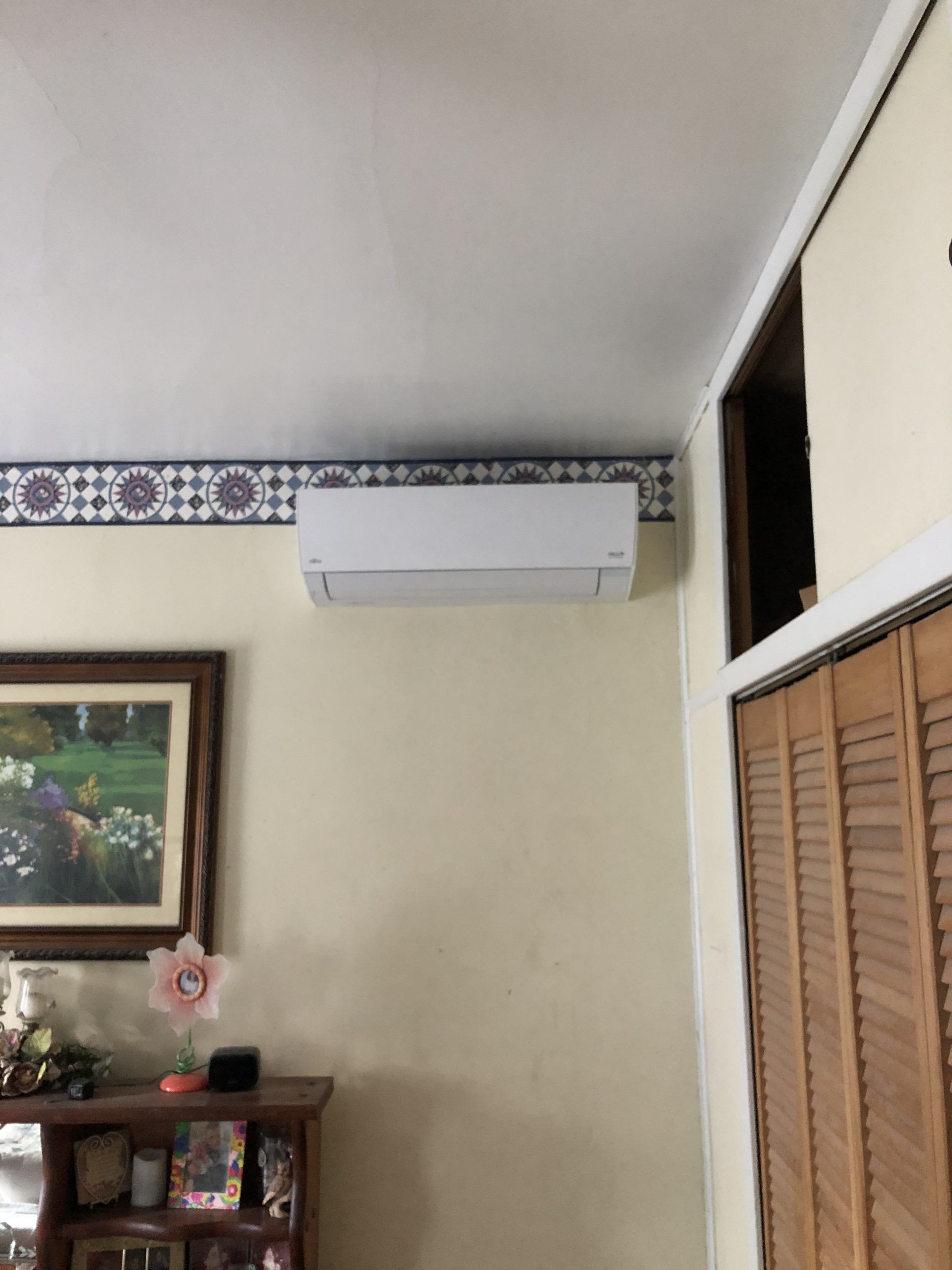 White wall-mounted air conditioner unit in a room with a patterned border, next to a wooden door.