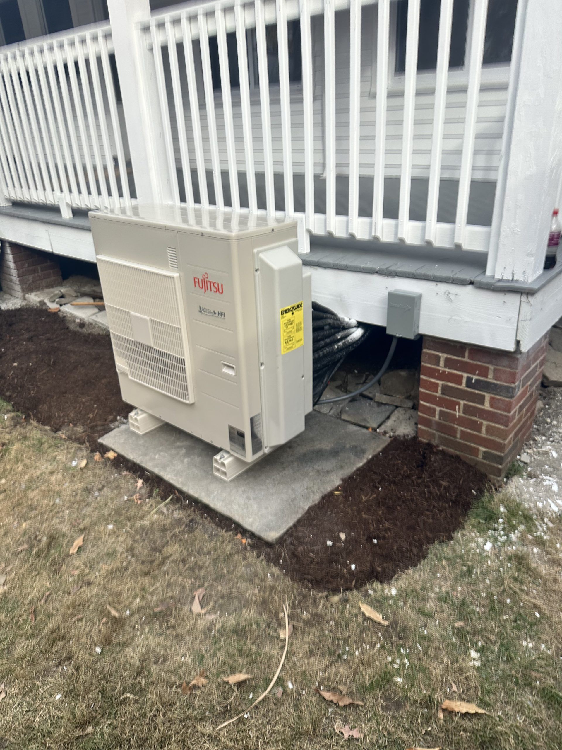 Air conditioning unit outside a white house with a brick base.