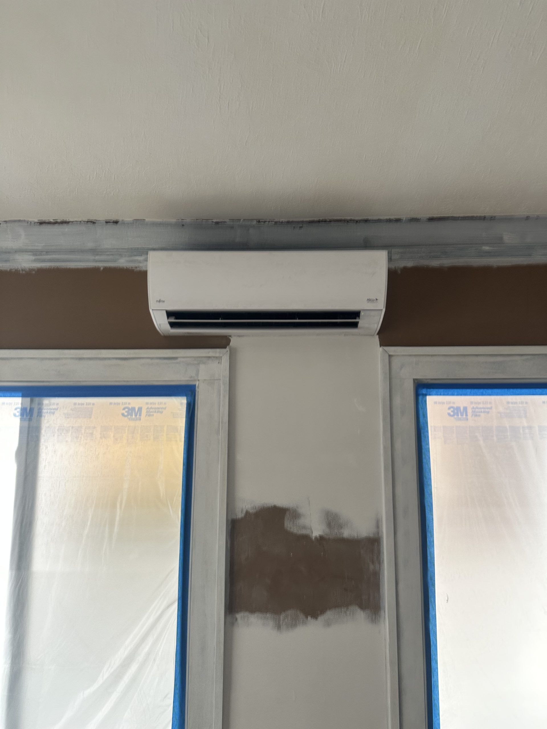 White air conditioning unit mounted on a wall between two window frames.