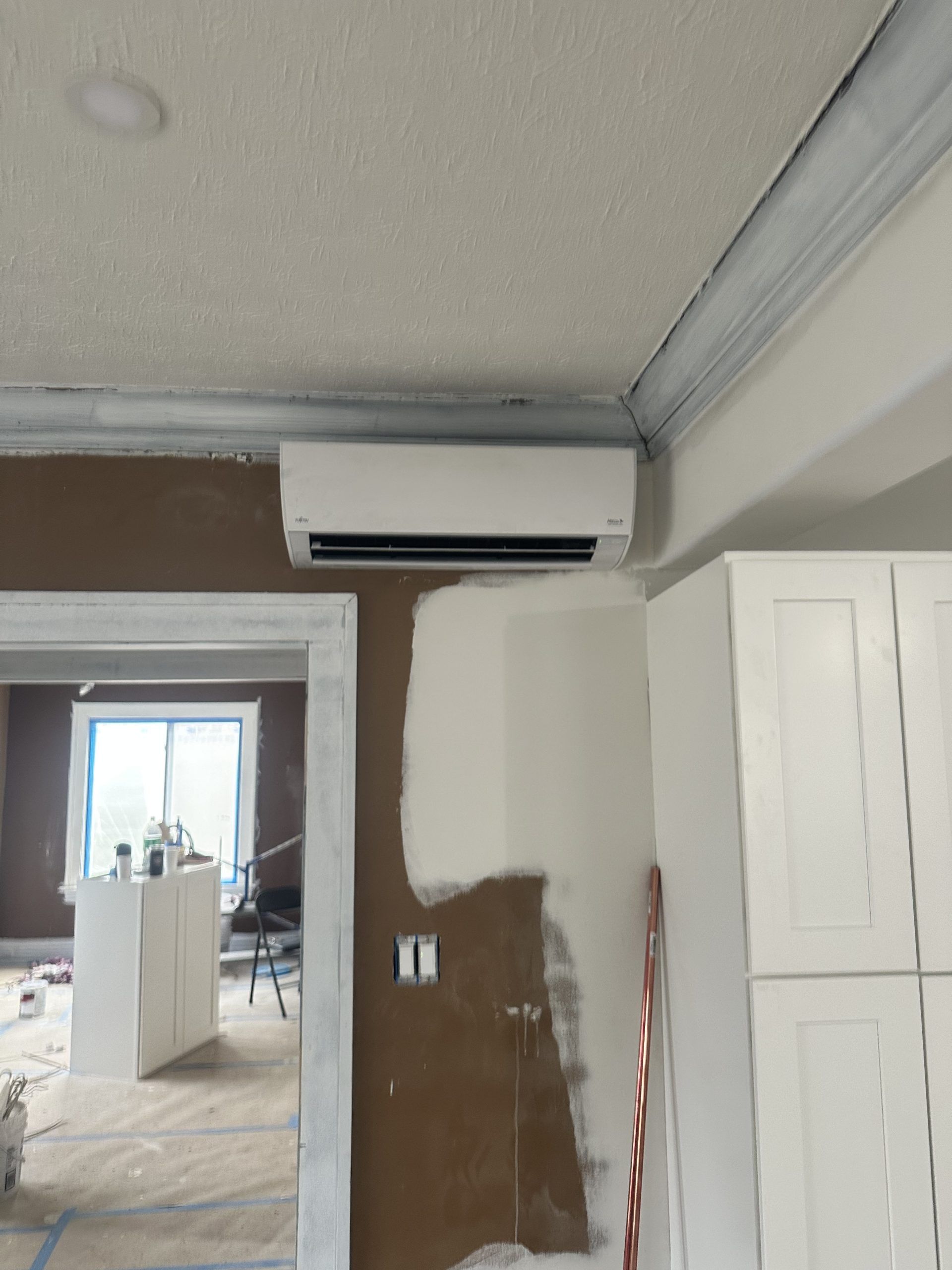 White HVAC unit installed near a ceiling in a room with white cabinets and a doorway.