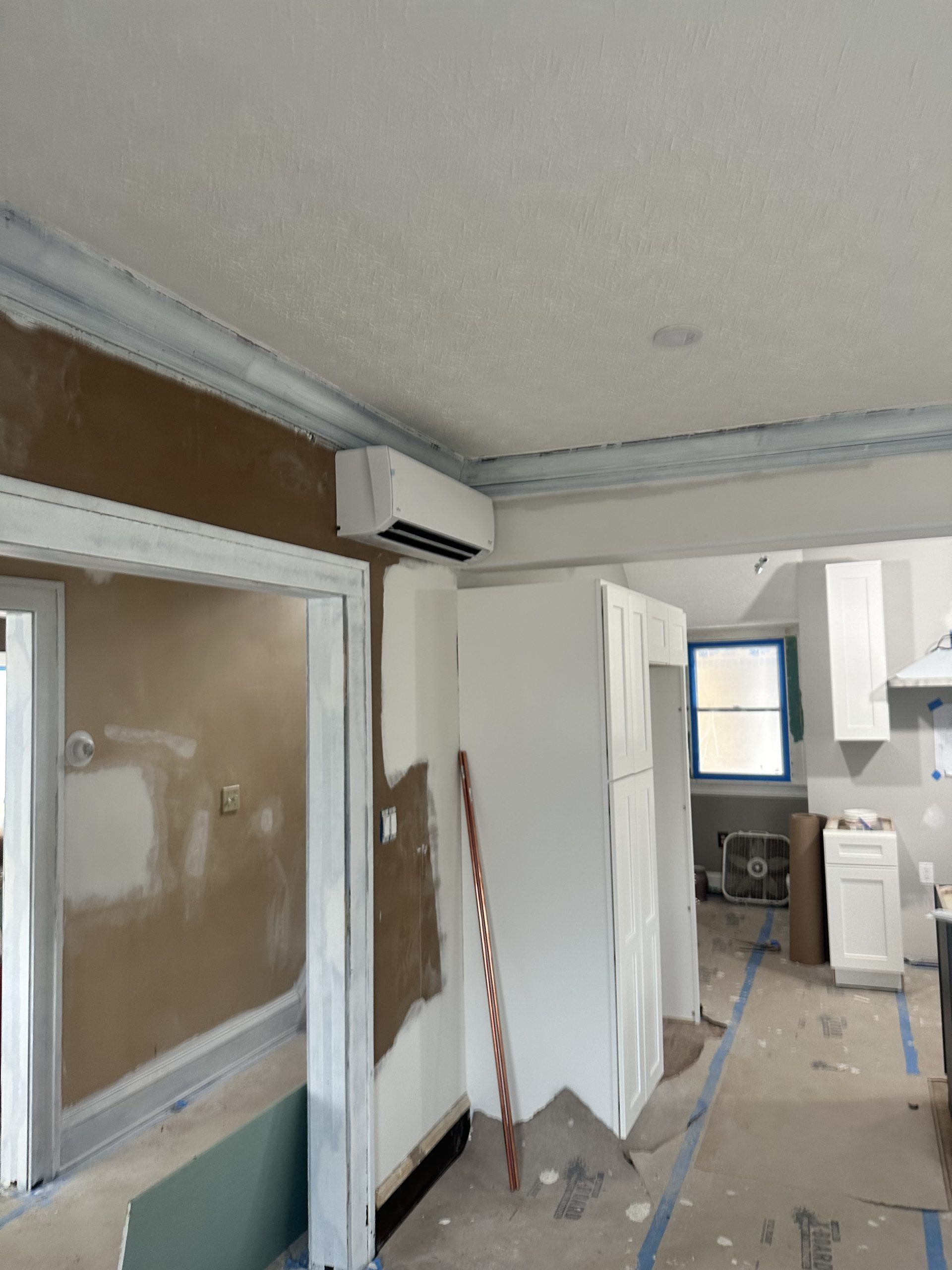 Interior kitchen undergoing renovation, air conditioning unit mounted on wall, cabinetry in place