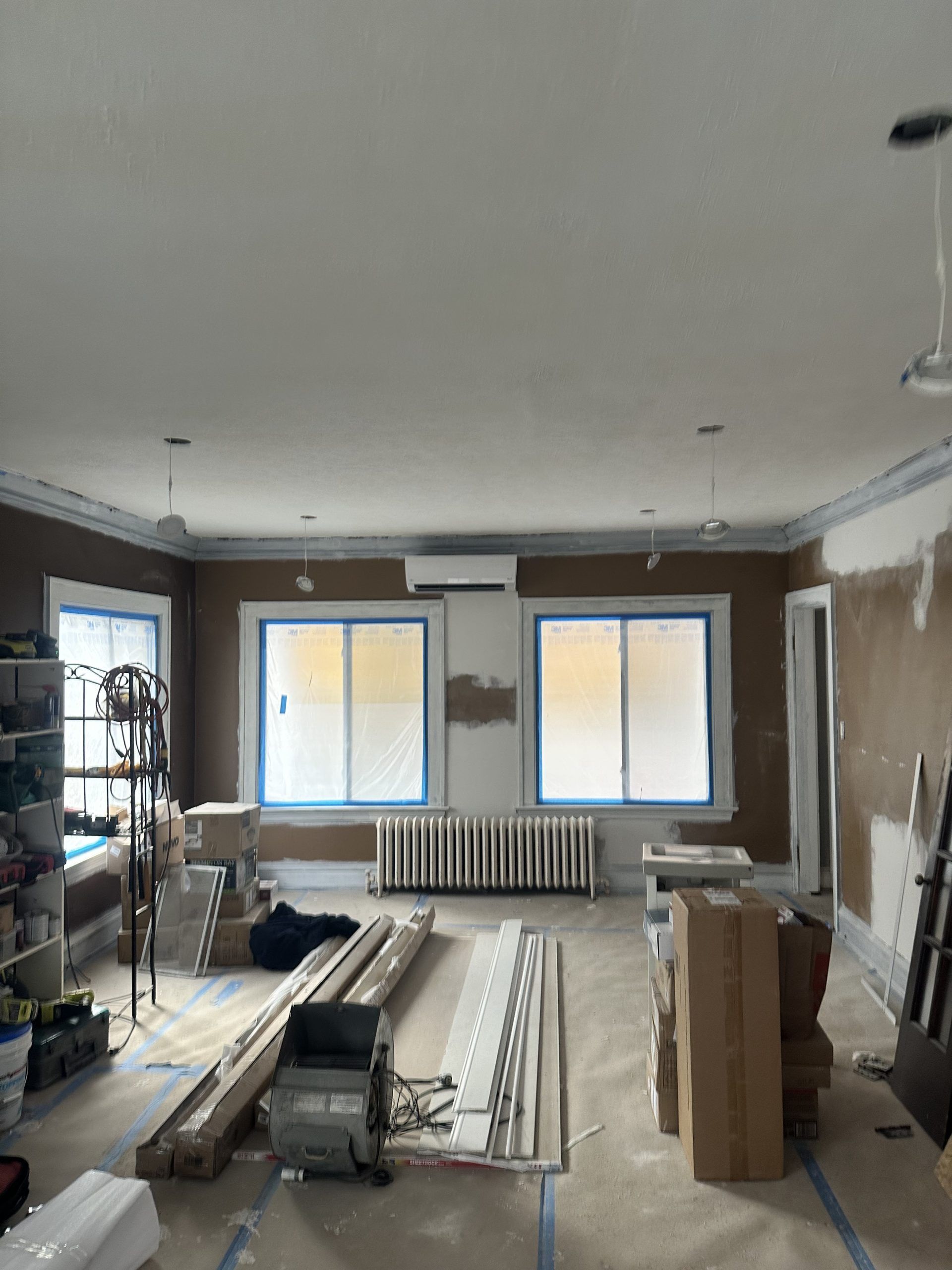 Interior room under construction, with windows covered, brown walls, and materials on the floor.