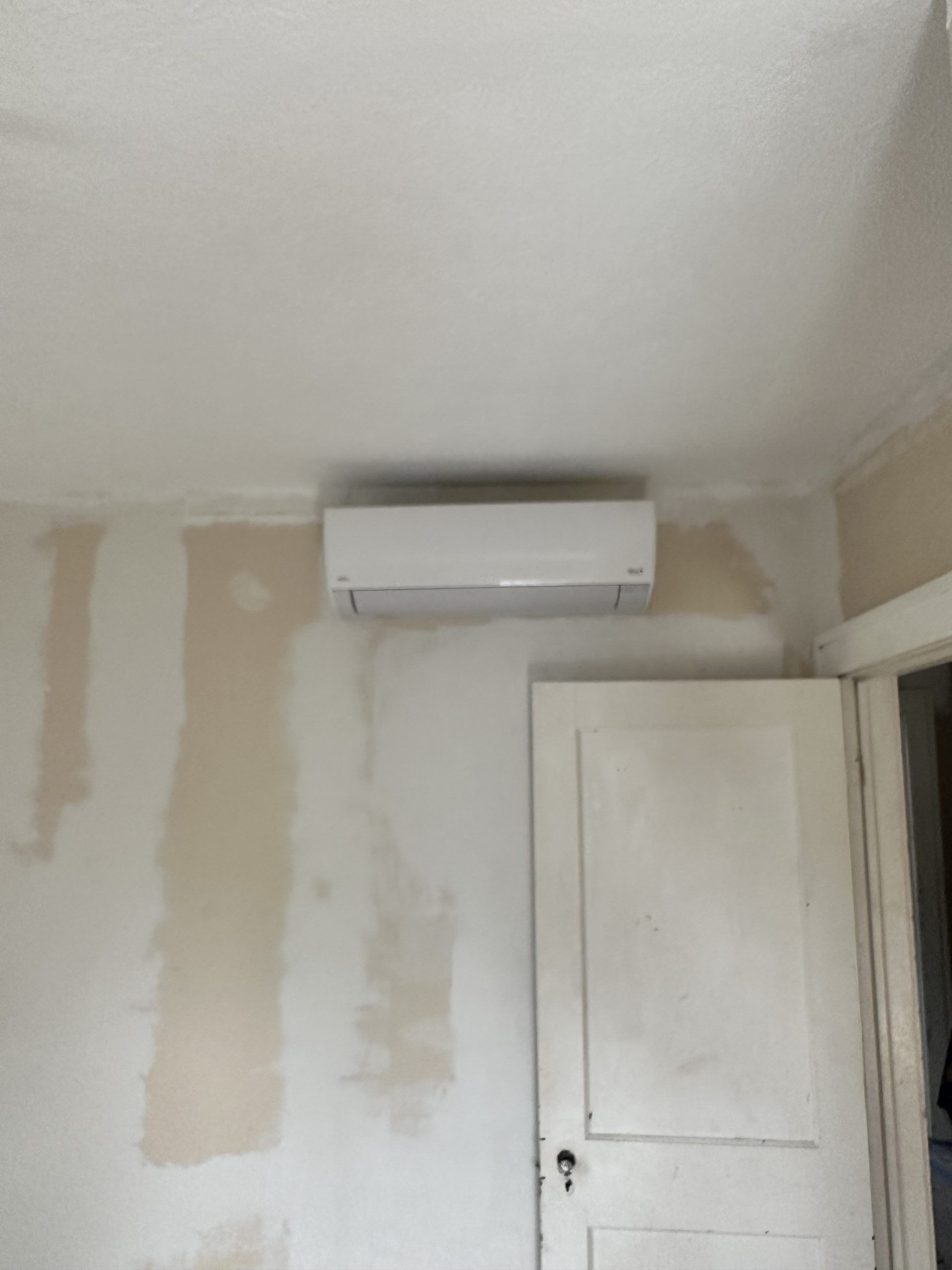 White ductless air conditioner mounted on a wall above a white door; drywall visible.