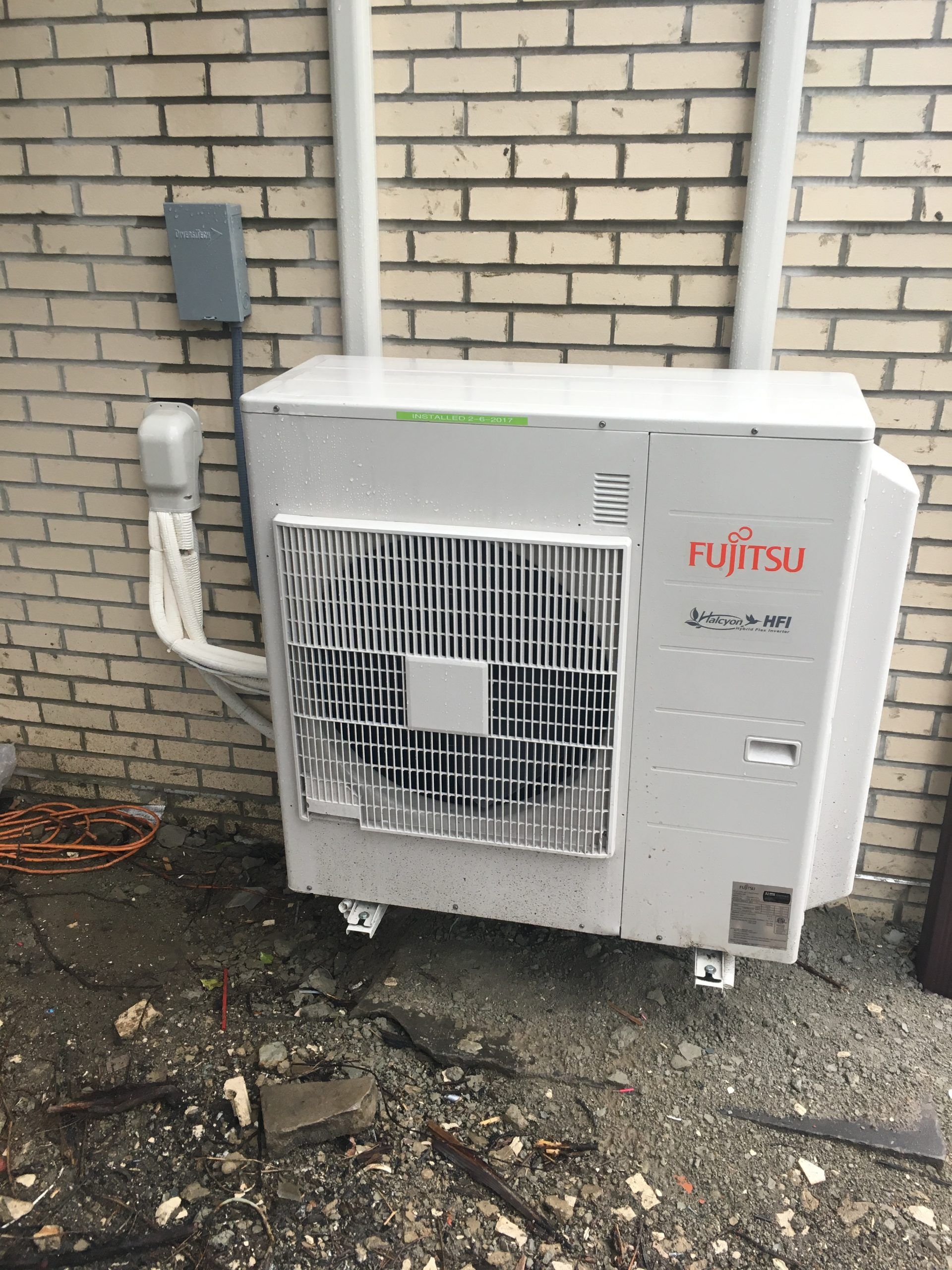 Fujitsu heat pump mounted on a brick wall, electrical box above.