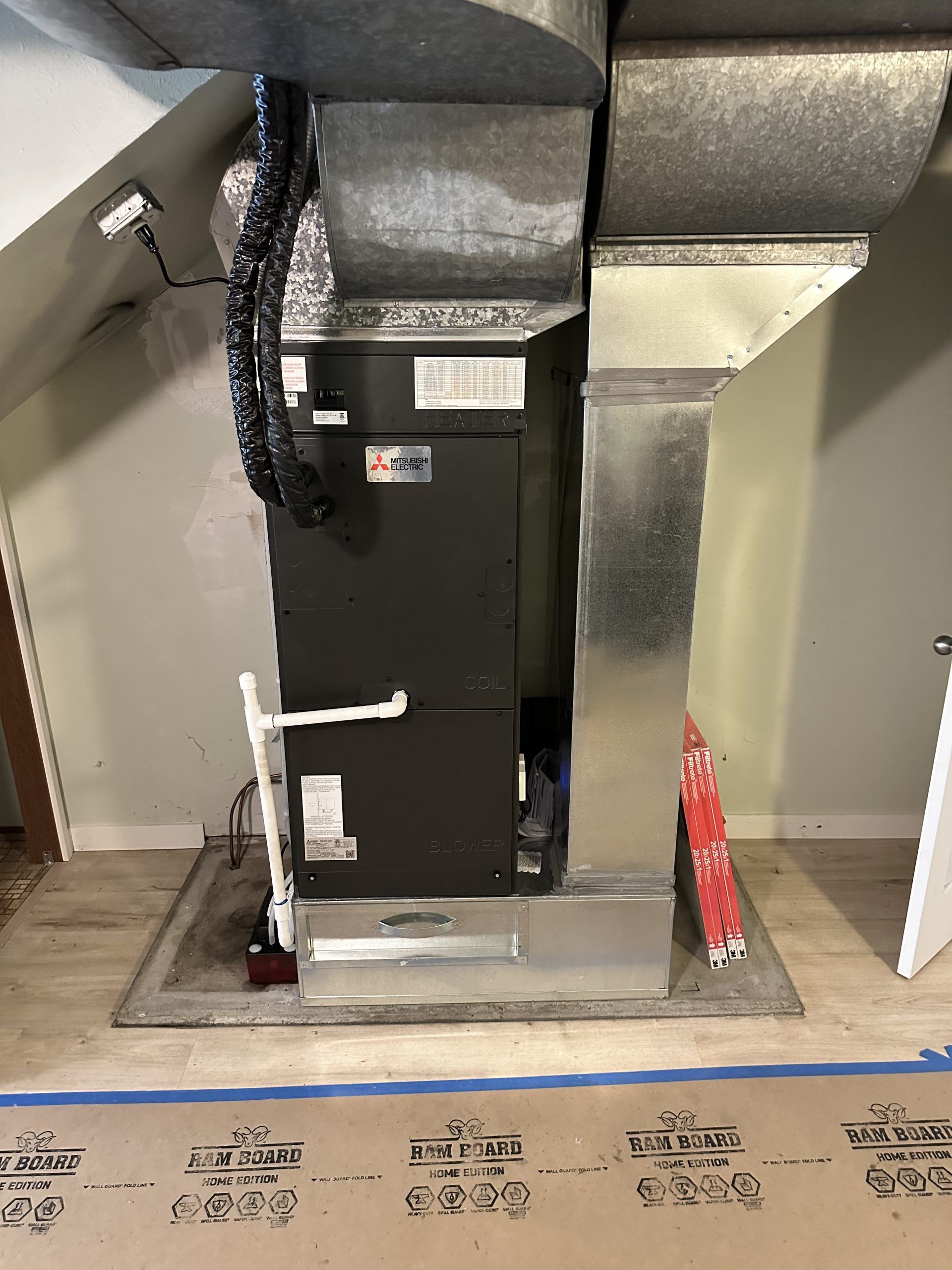 Furnace with ducts and pipes in an attic or utility room. Metal and black components against light walls.