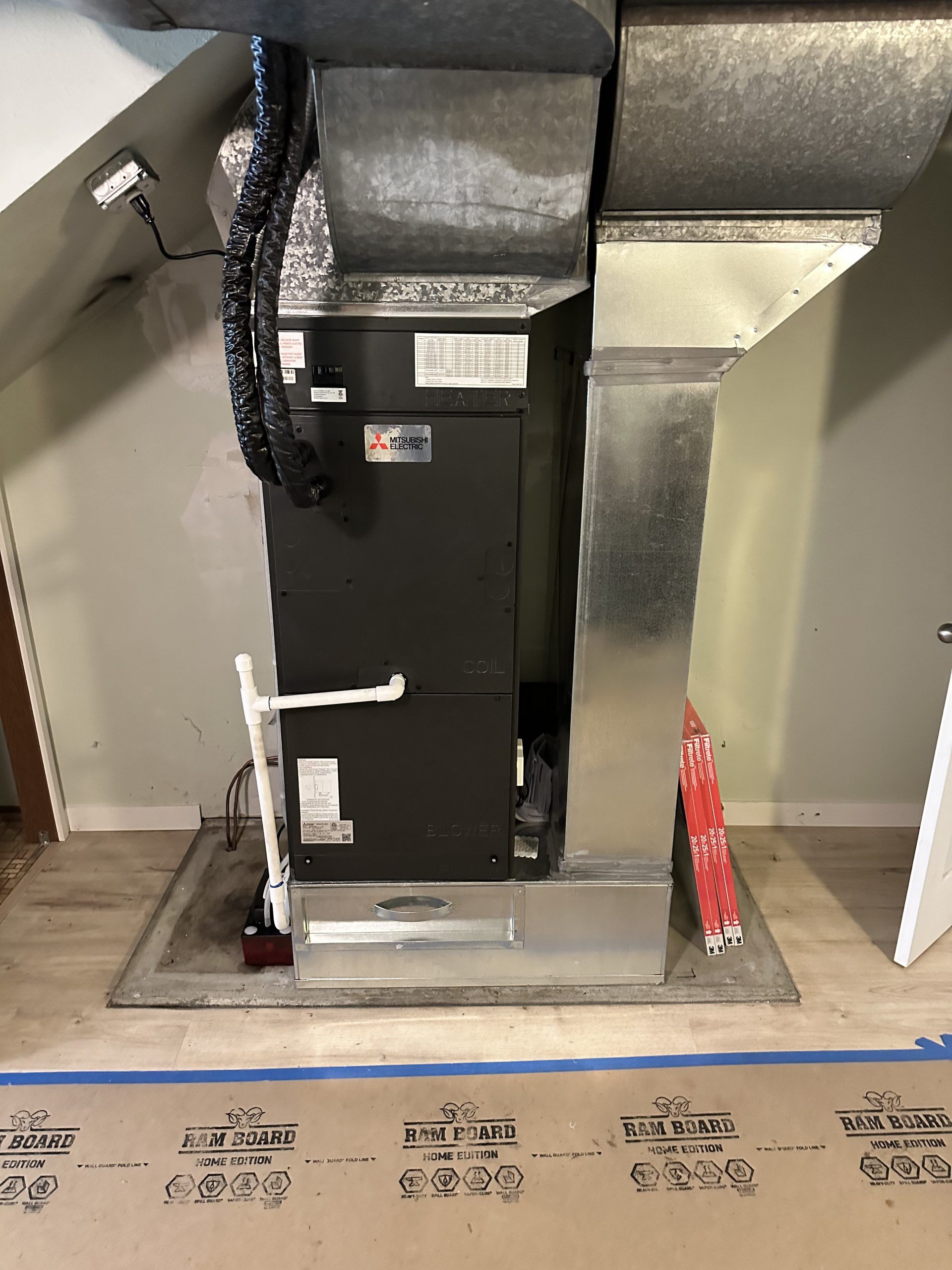 Furnace system in a home; black unit with metal ductwork and a white pipe.