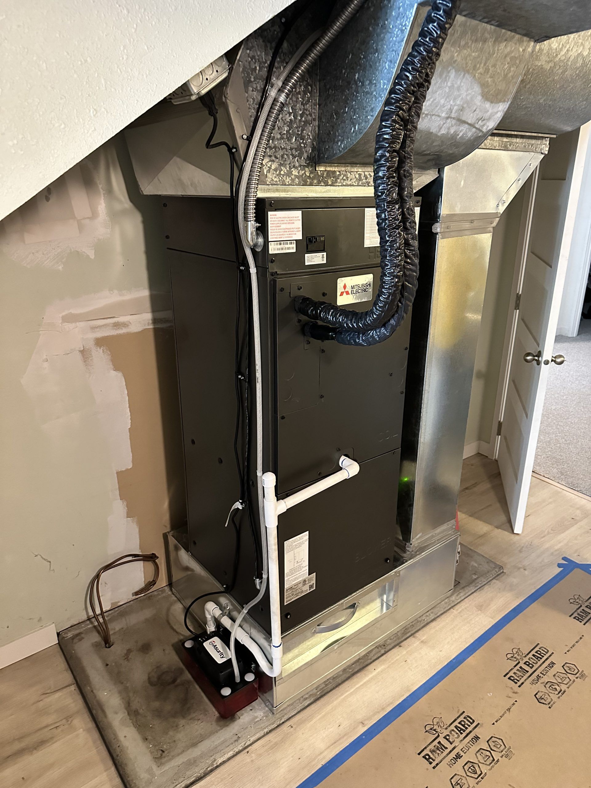 HVAC unit in a small alcove, with ductwork and piping. Black and silver with a beige wall.