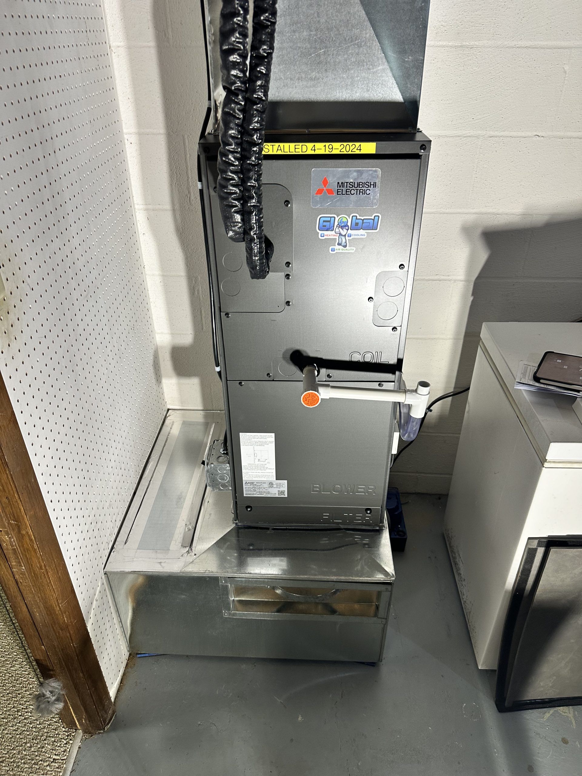 Furnace in a basement, mounted on a metal platform. Ductwork above. Grey, silver, and black.
