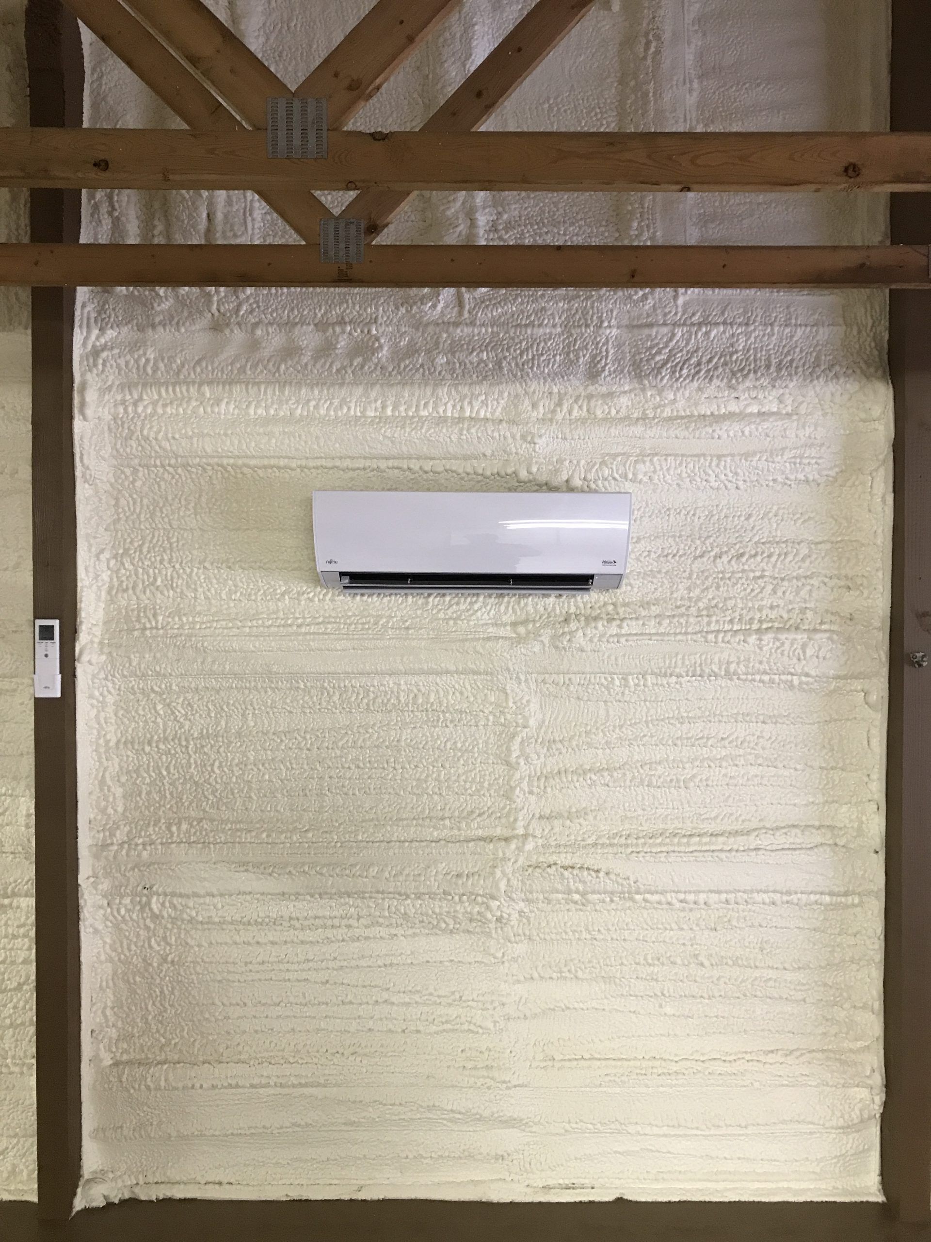 White air conditioner on insulated wall in a wooden-framed structure.
