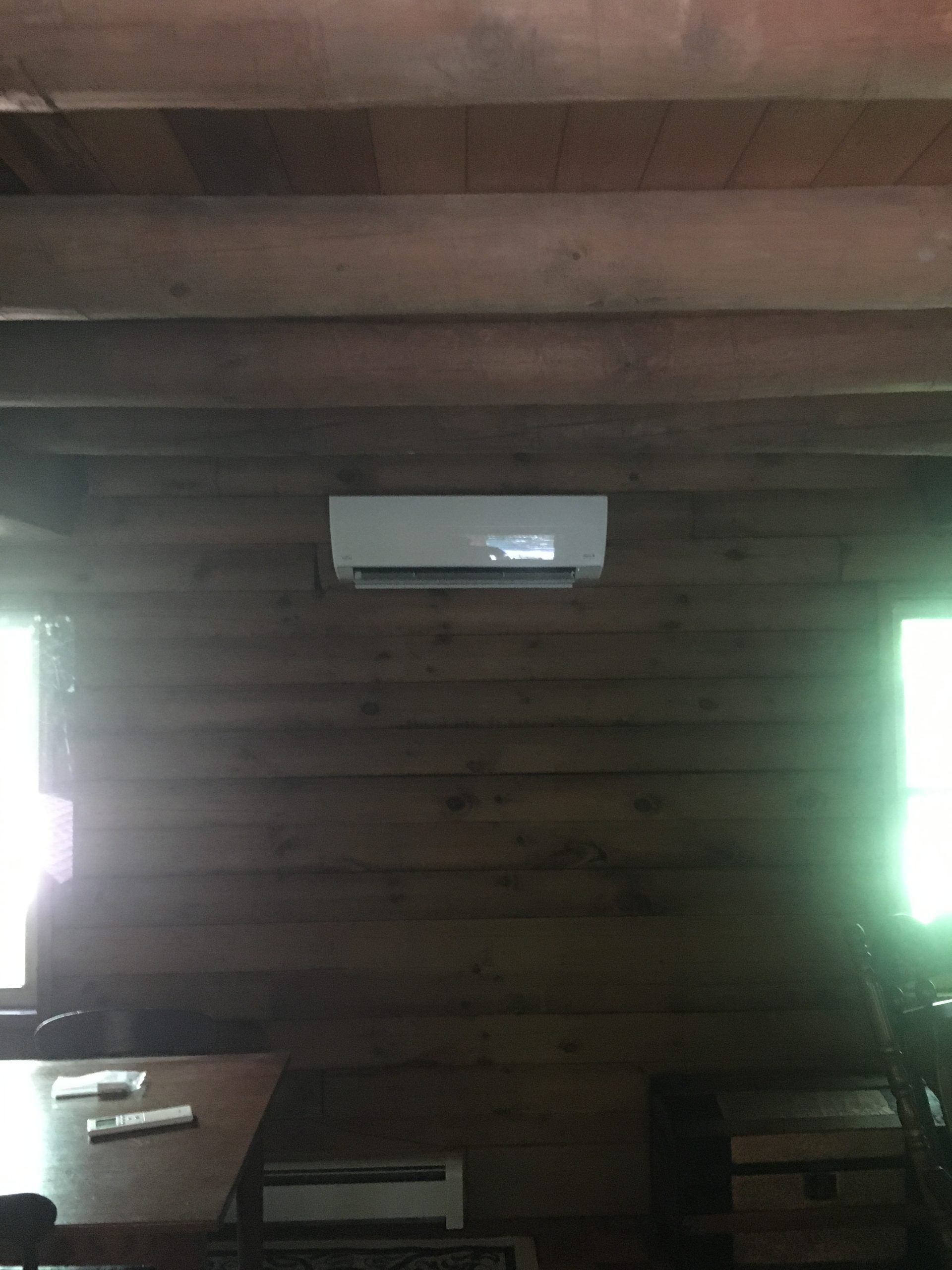 A white air conditioner mounted on a wooden wall inside a room with wooden beams.