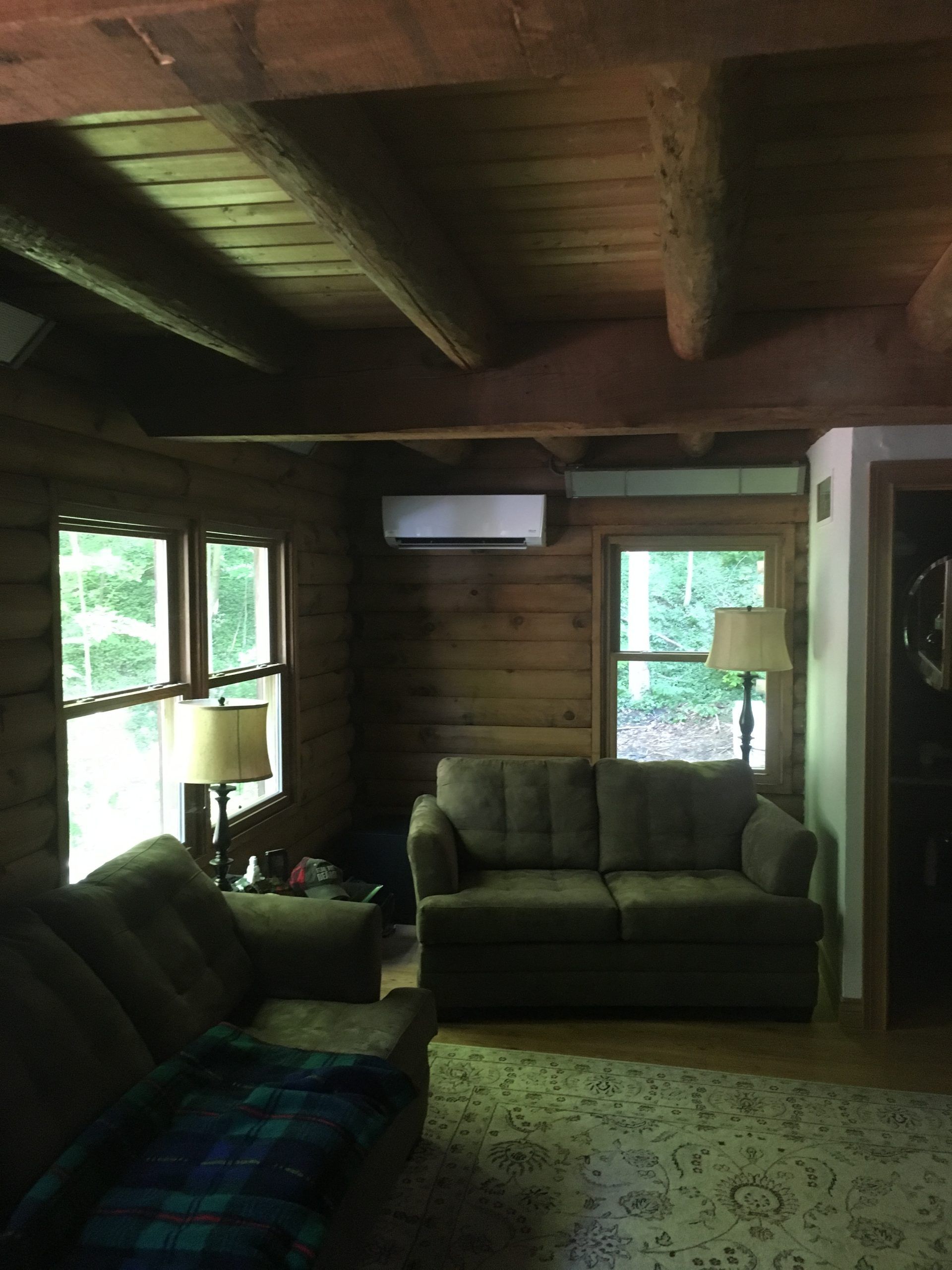 Cozy living room with log walls, two sofas, windows, and an air conditioning unit.
