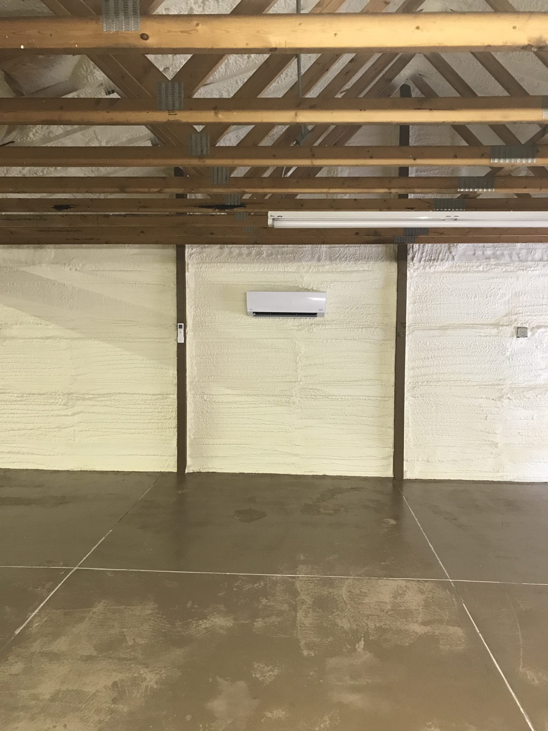 Interior of a building with spray foam insulation on the walls. An air conditioner is mounted in the center.