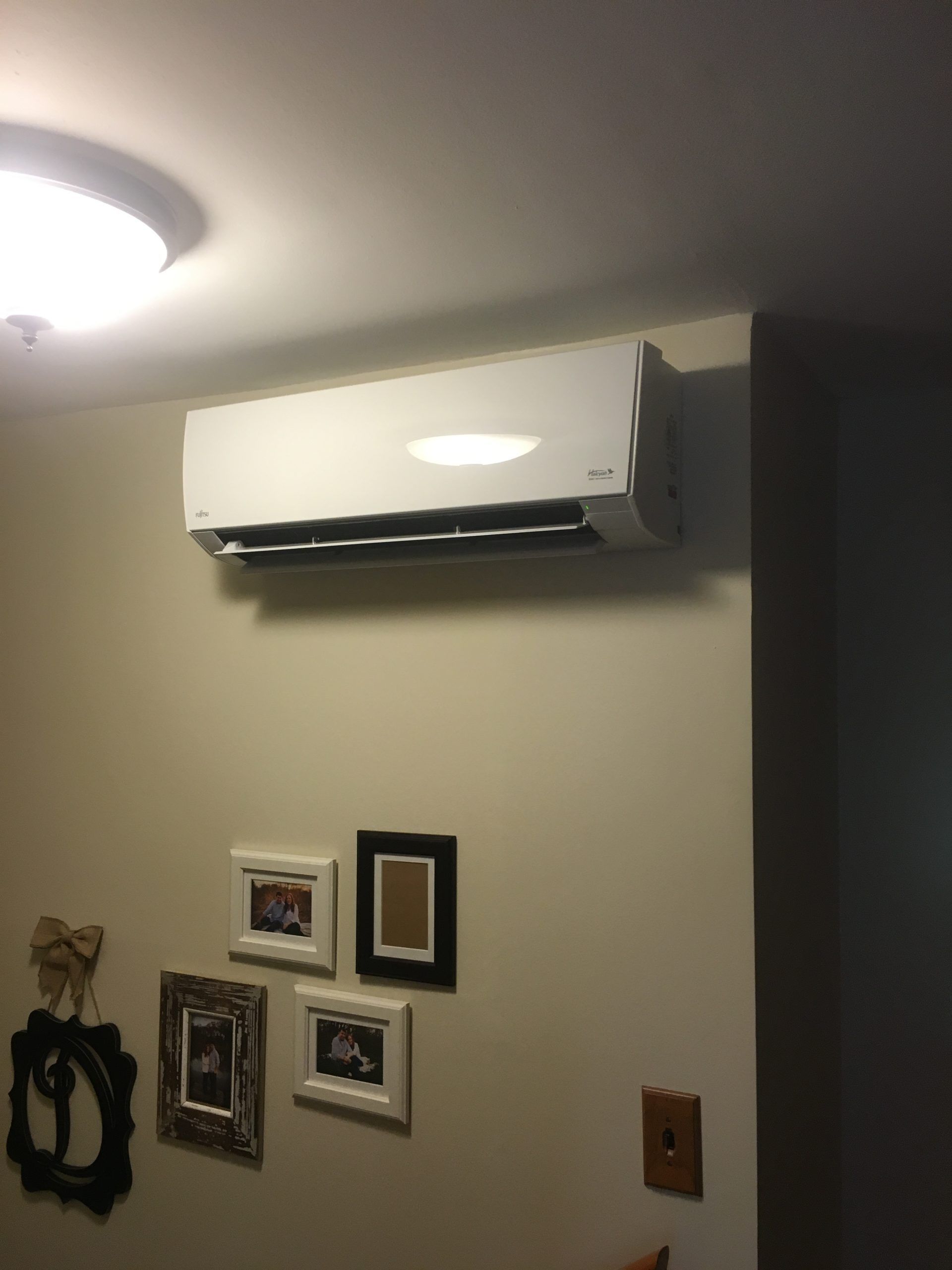 White air conditioning unit mounted on a beige wall, above several framed pictures.