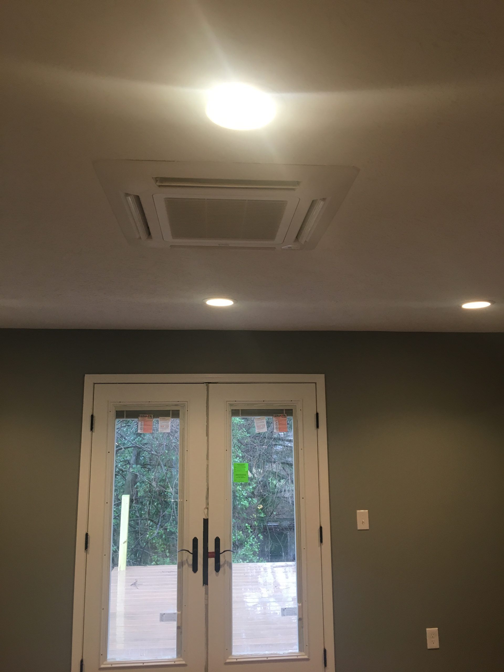 Ceiling-mounted HVAC unit above white double doors and recessed lighting in a room with gray walls.