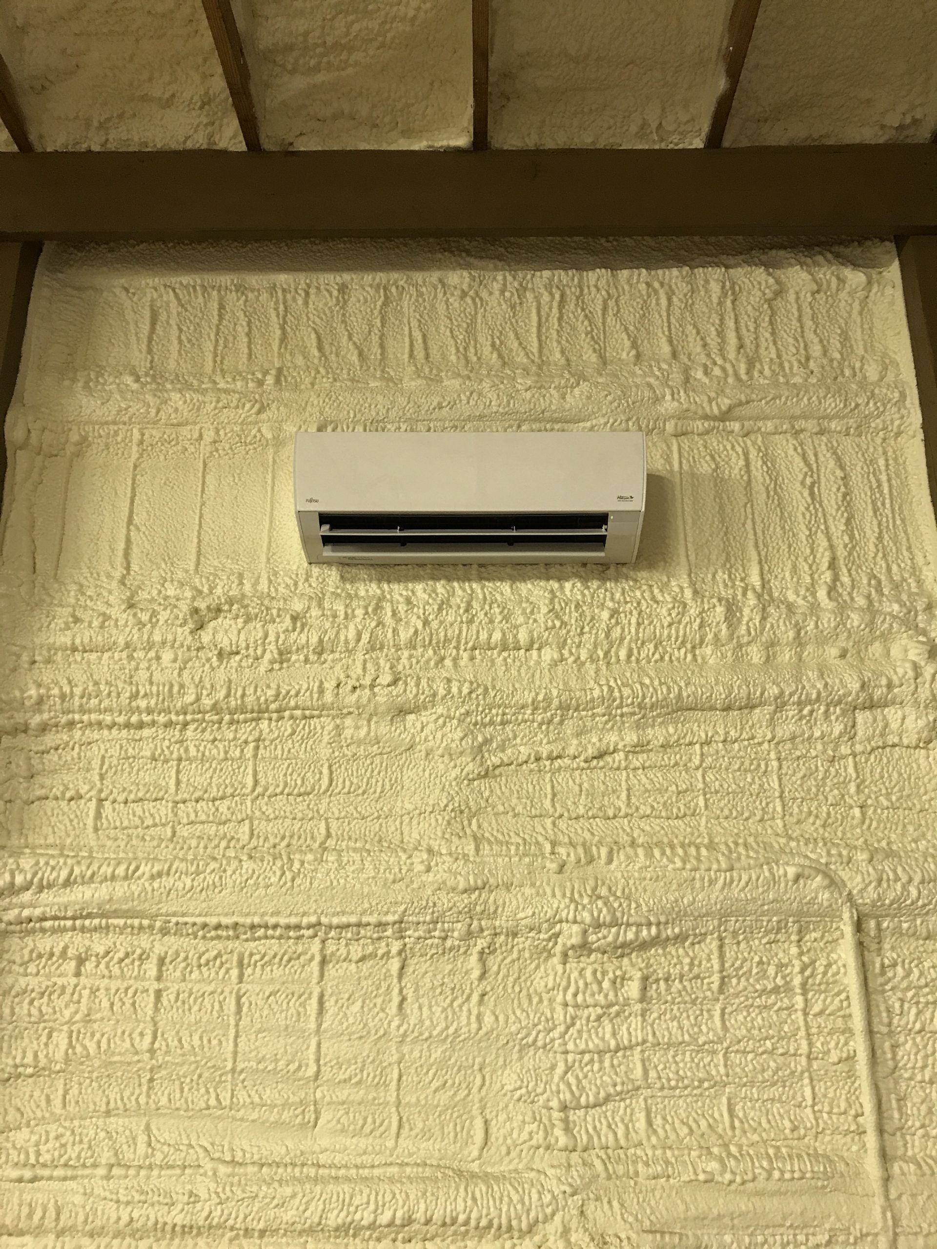White air conditioning unit mounted on a wall covered in textured yellow insulation.