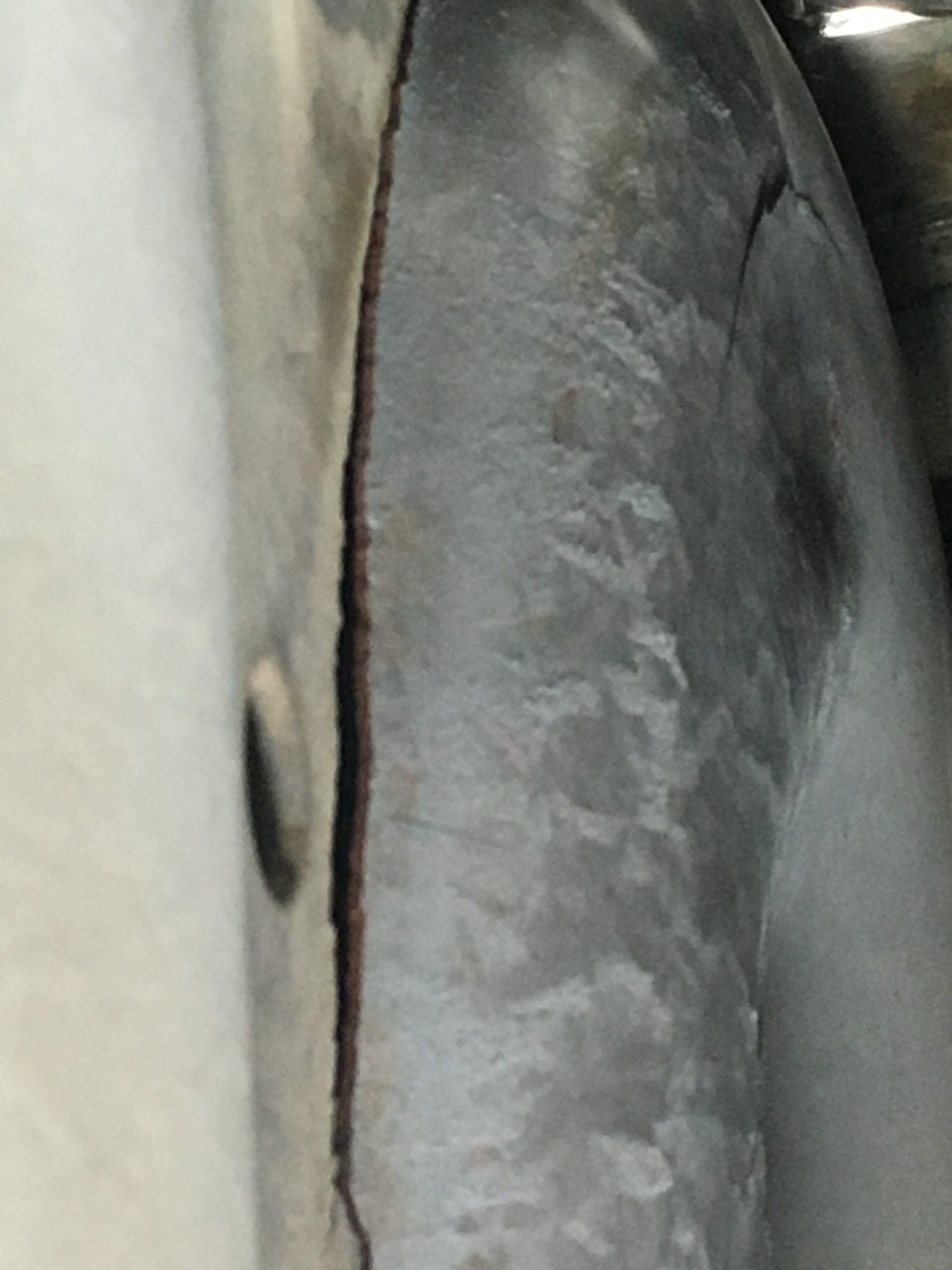 Close-up view of a metal component with a long crack running vertically, likely due to stress.