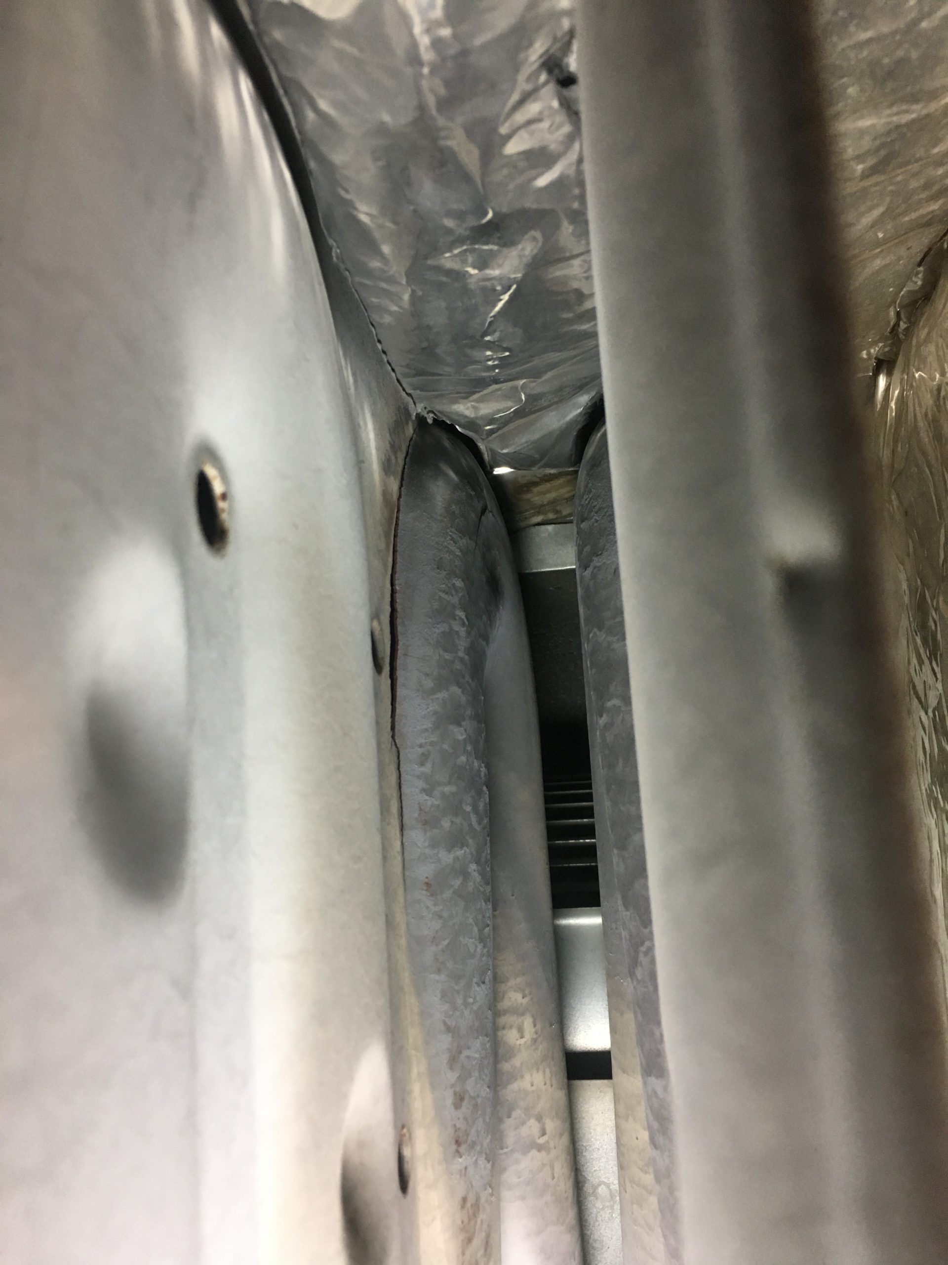 Looking into a dark cavity between two metal structures, possibly ductwork. Gray, industrial setting.