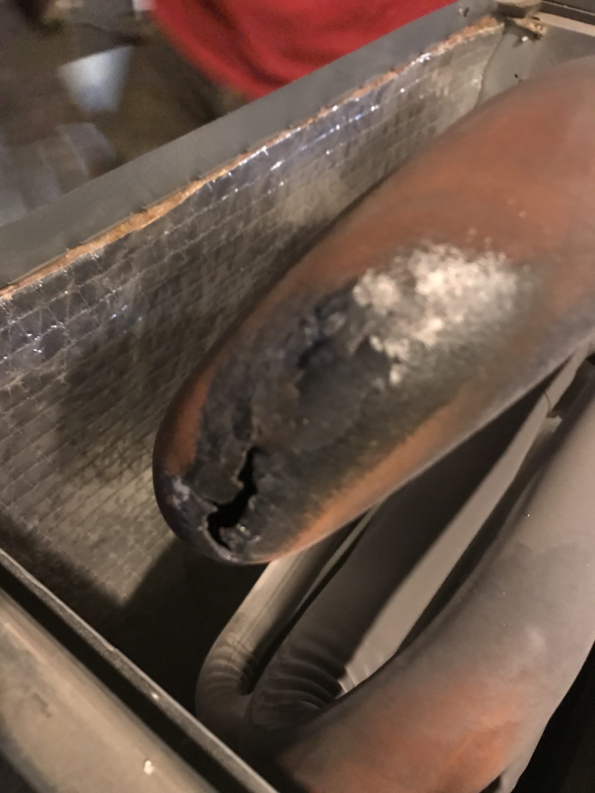 Damaged copper pipe with a burnt, cracked end inside a metal enclosure.