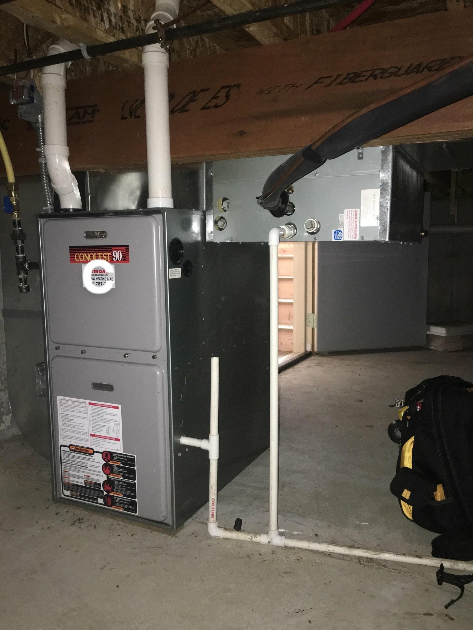Furnace in a basement, with attached pipes and ductwork. Grey and white colors.