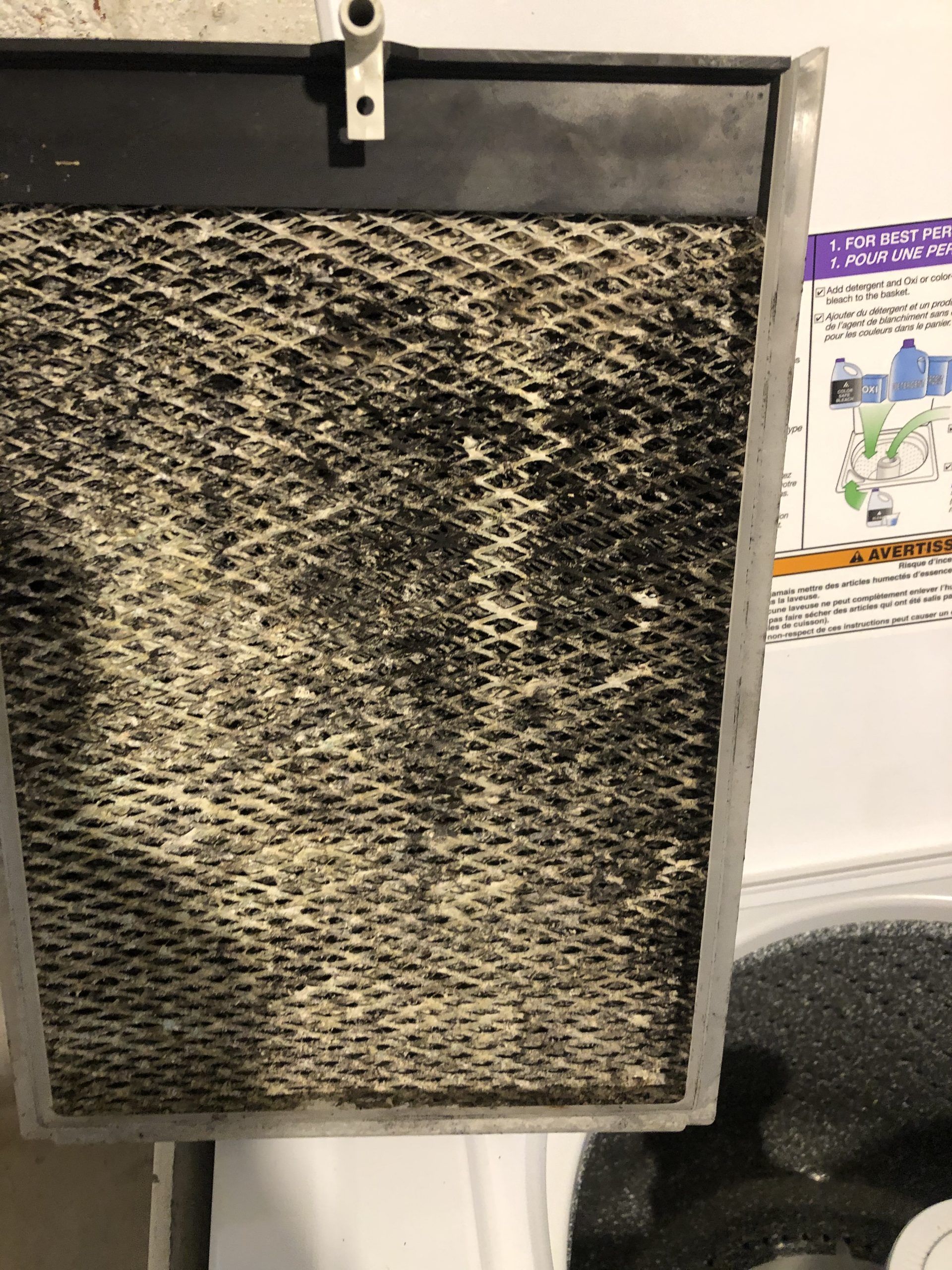 Dirty air filter with a honeycomb-like pattern, covered in dark and light debris, in a metal frame.